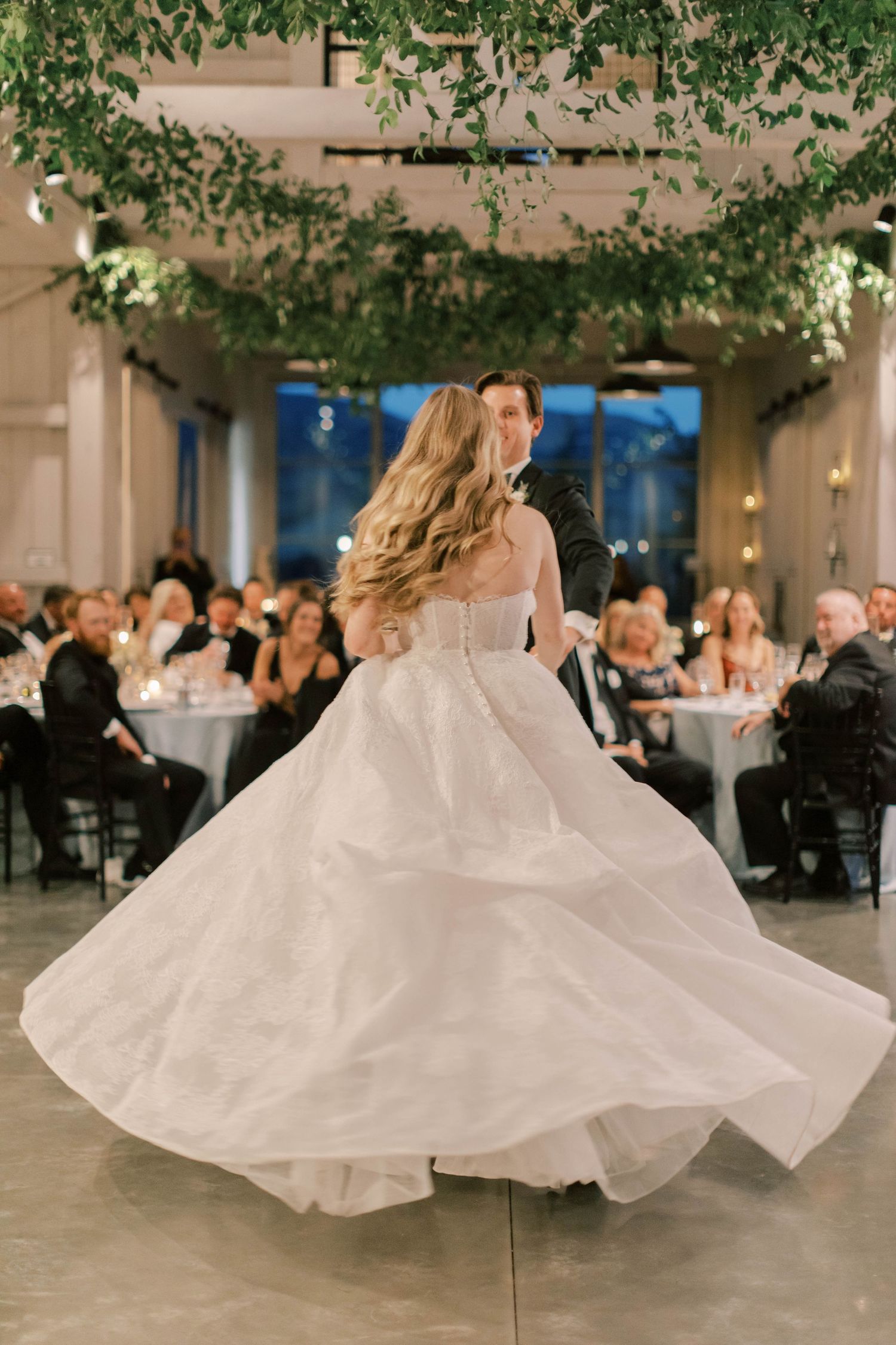 A bride in a flowing white gown twirls on the dance floor during her wedding reception.