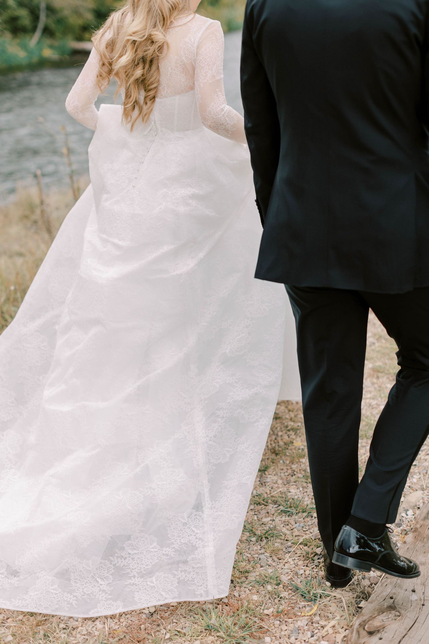 Detail shot of bride's flowing white dress train next to groom's formal black tuxedo.