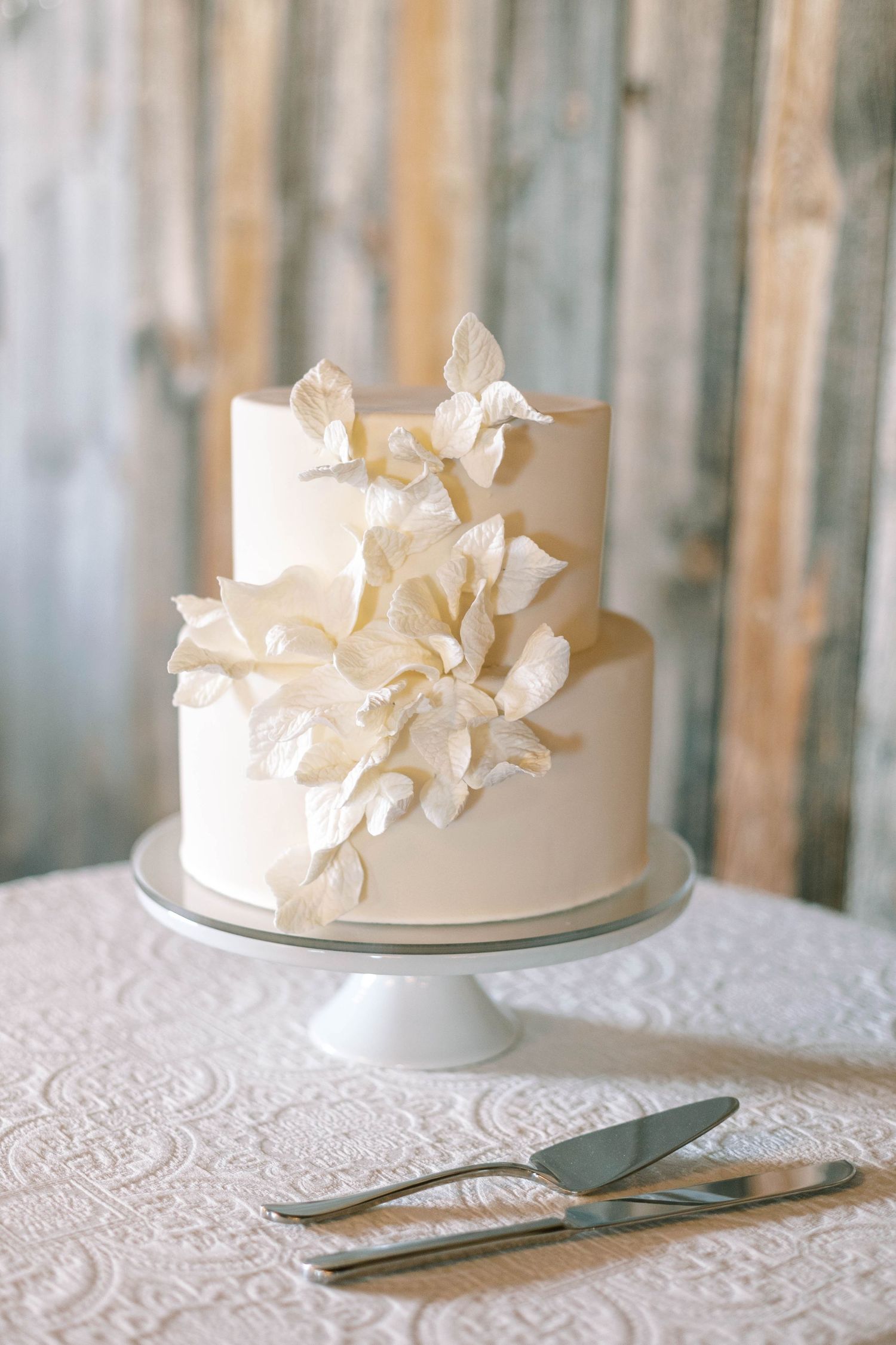Simple white two-tier wedding cake decorated with delicate sugar flowers on a silver cake stand.