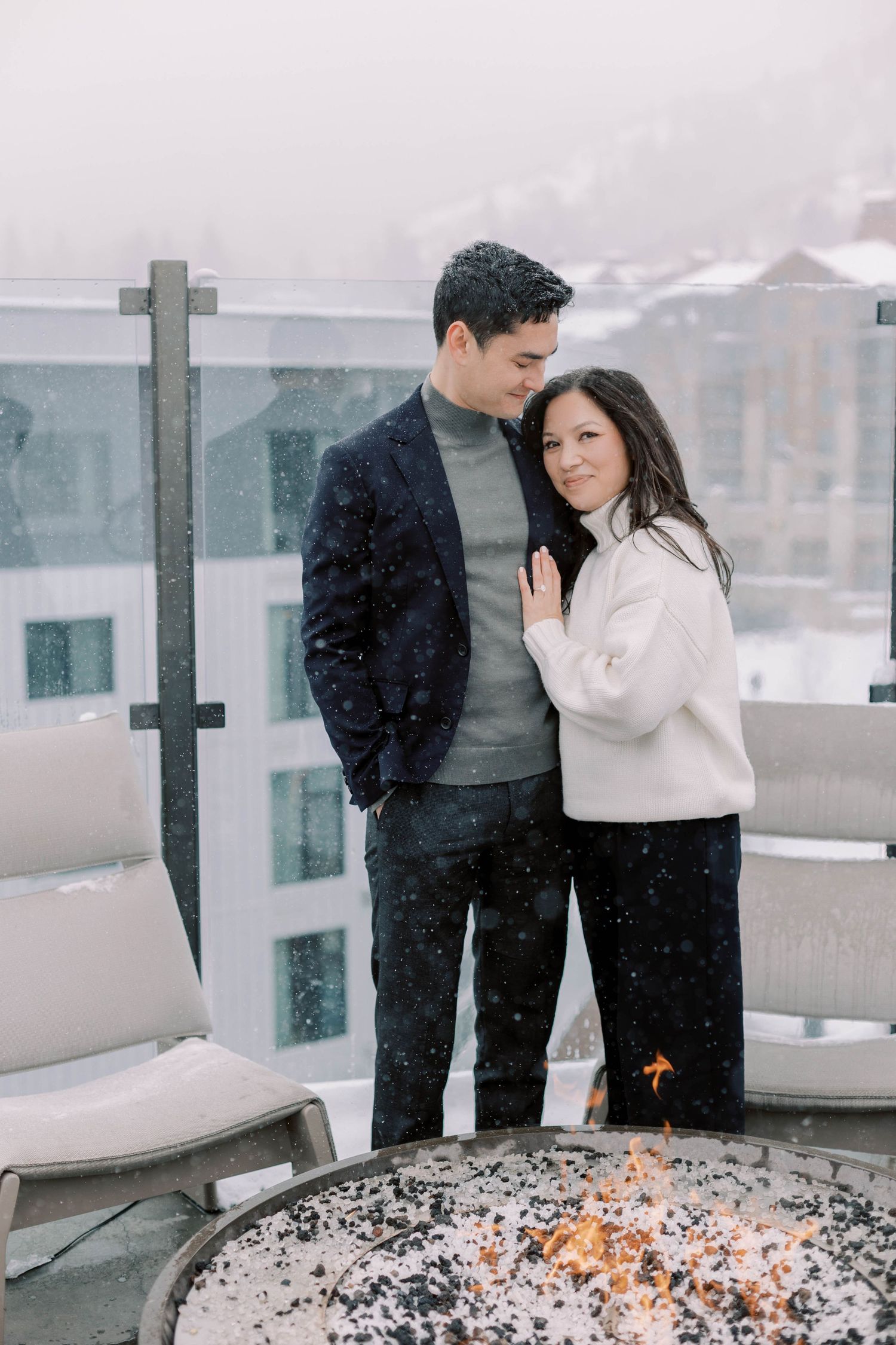Couple standing by outdoor fire pit during snowfall at the pendry park city.