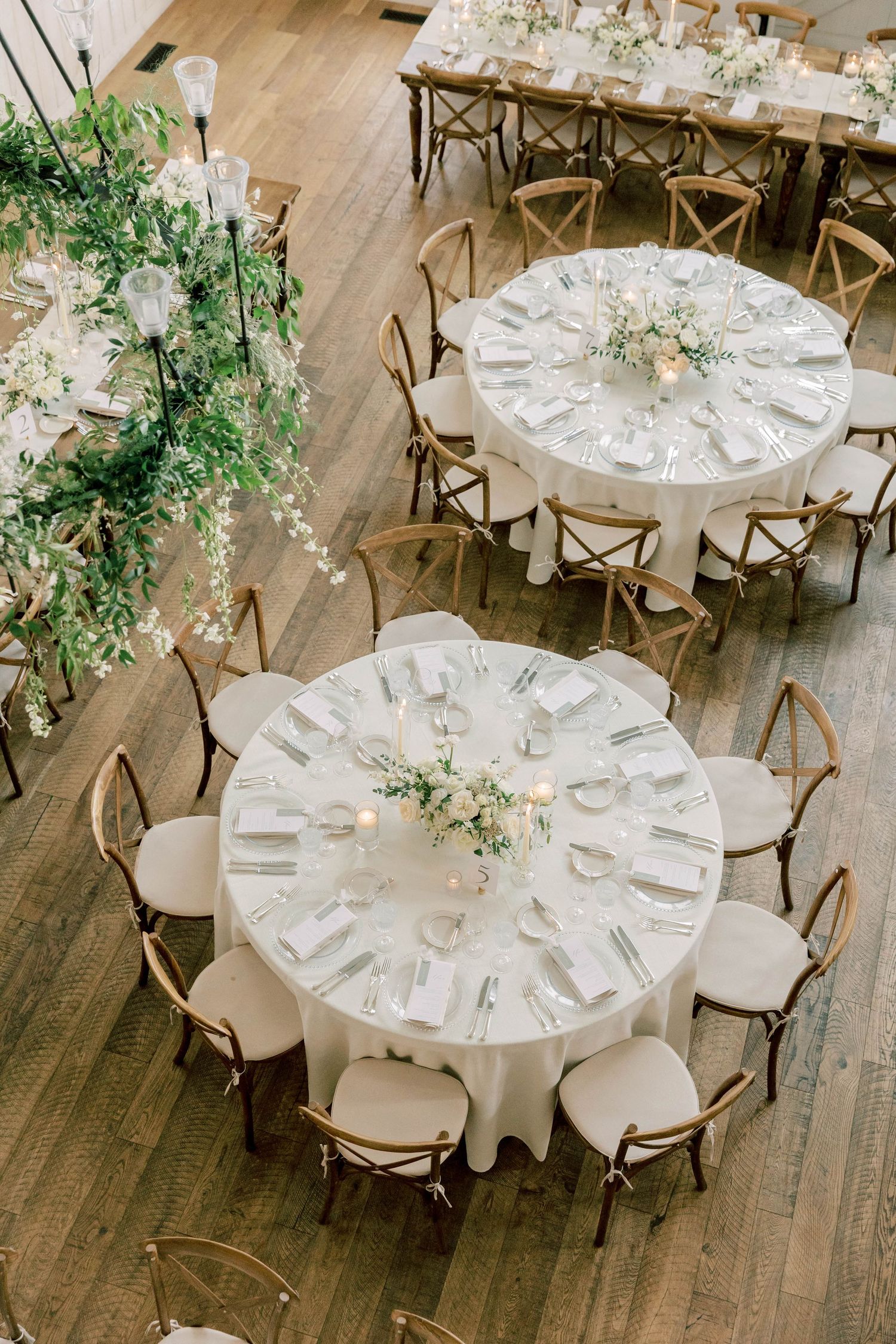 Overhead view of round reception tables with white linens and cross-back chairs.