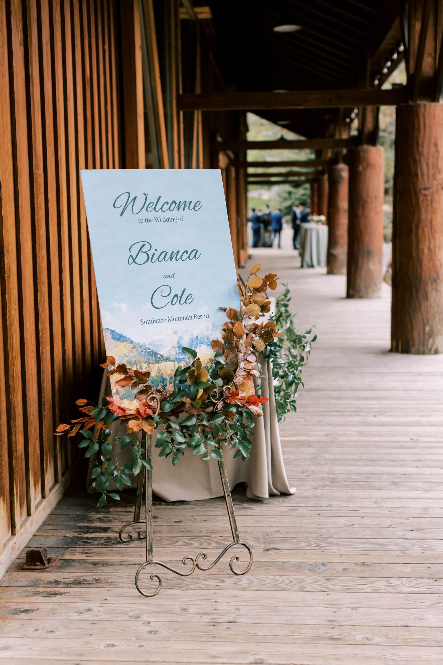 Wedding welcome sign decorated with autumn foliage on a rustic wooden porch.