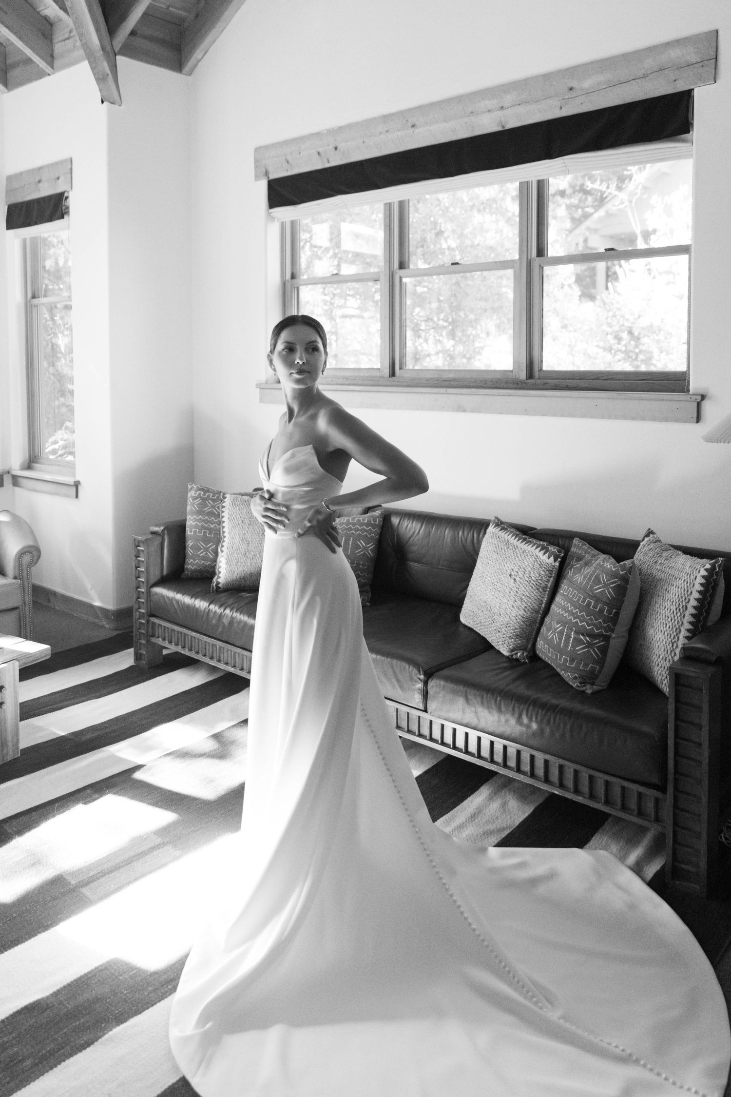 Black and white photo of an elegant wedding dress with long train in a rustic room.