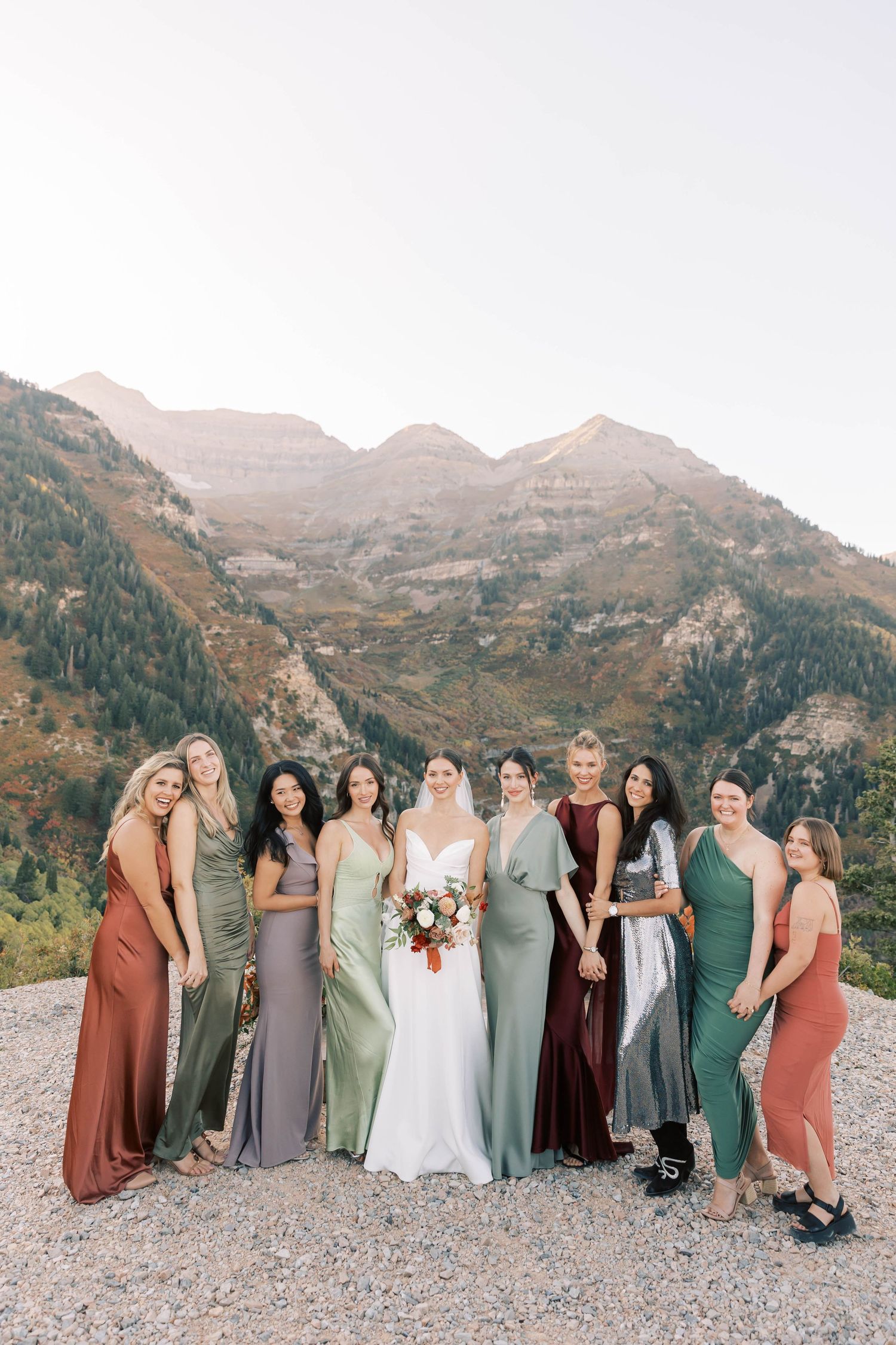 Wedding party in coordinated dresses poses against dramatic mountain landscape.
