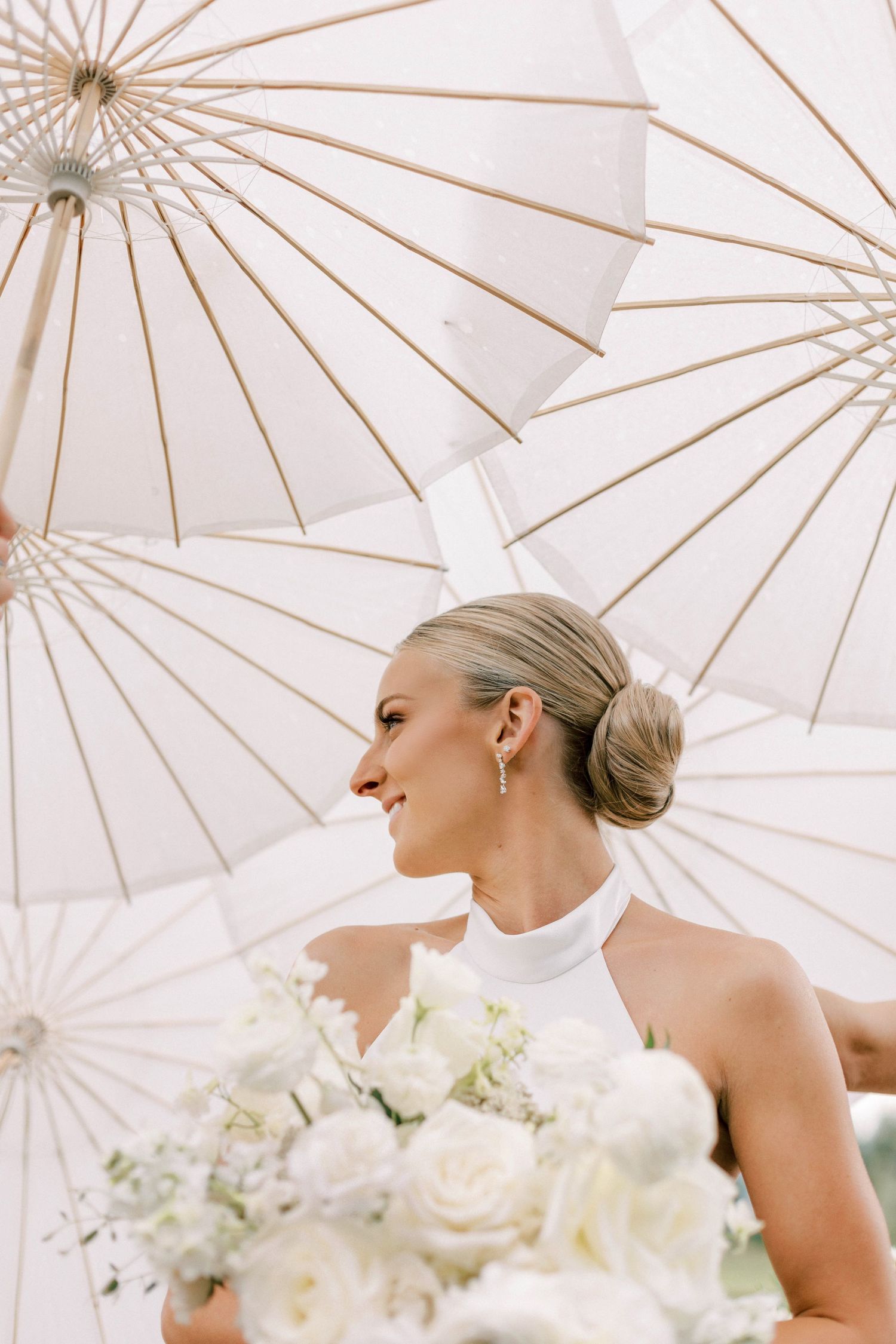 White paper parasols create elegant backdrop for bridal portrait with white bouquet.