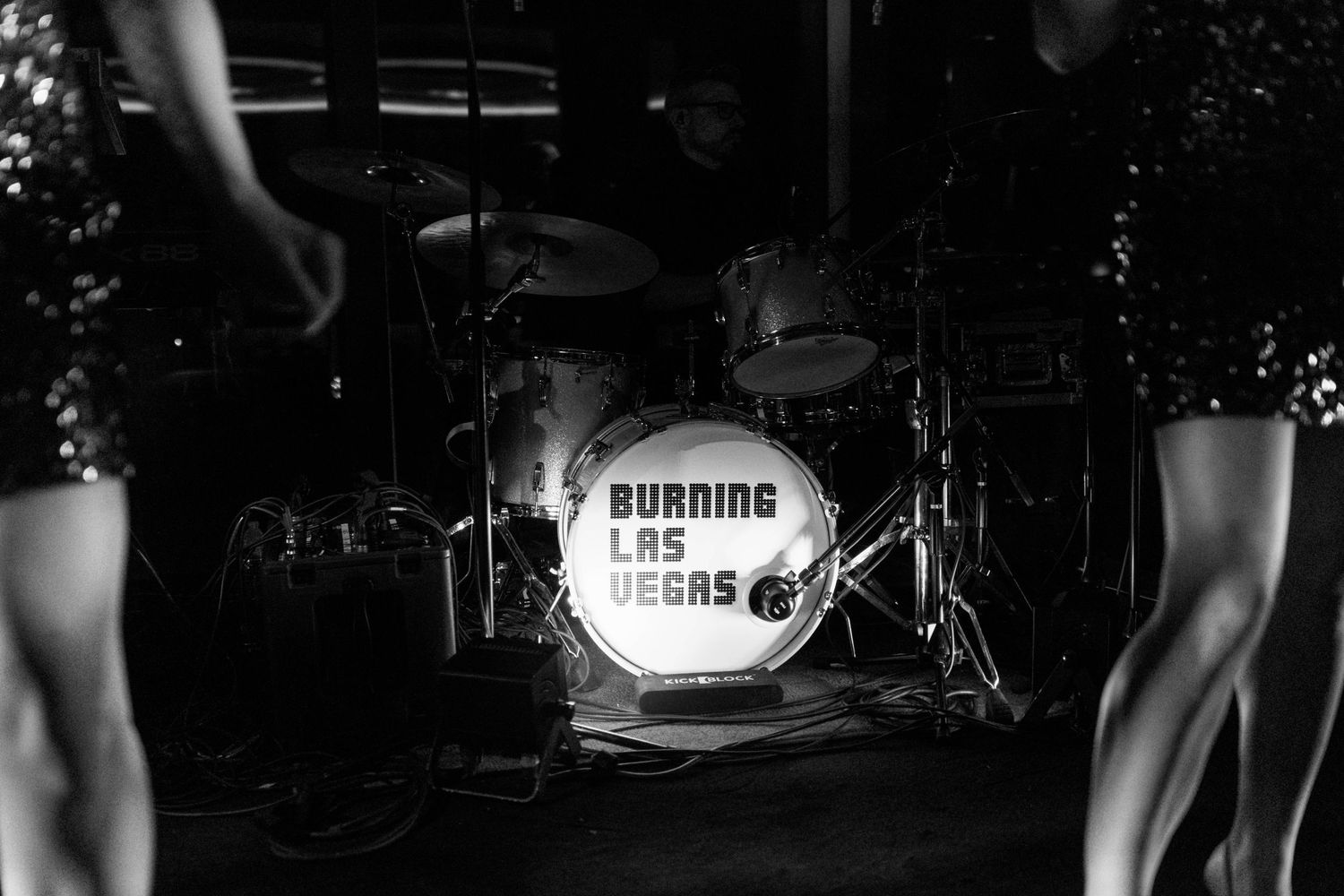 Black and white photo of a drum kit with 'Running Numbers' text illuminated on the bass drum.