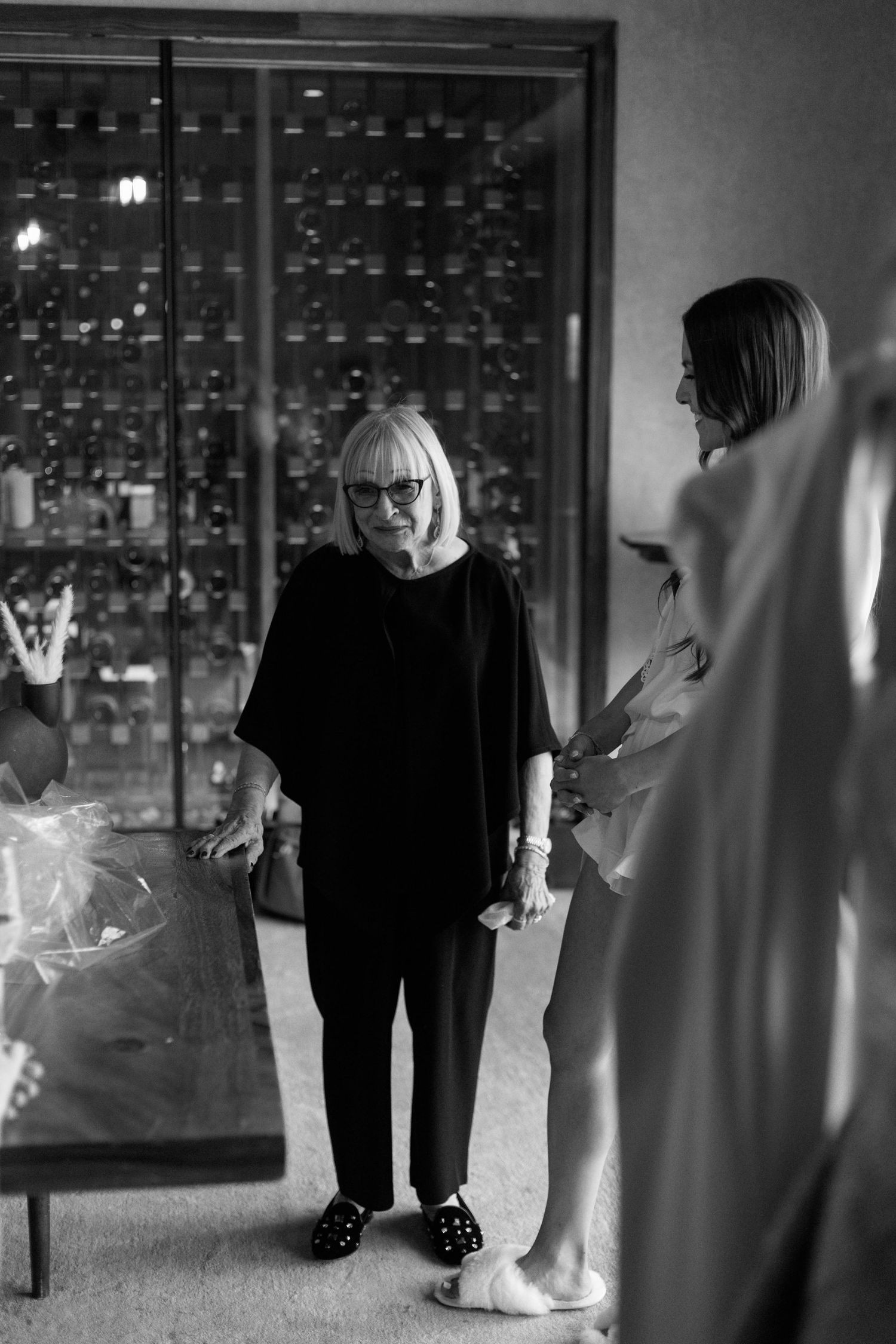 Black and white photo showing a wedding dress fitting scene with a display case in background.
