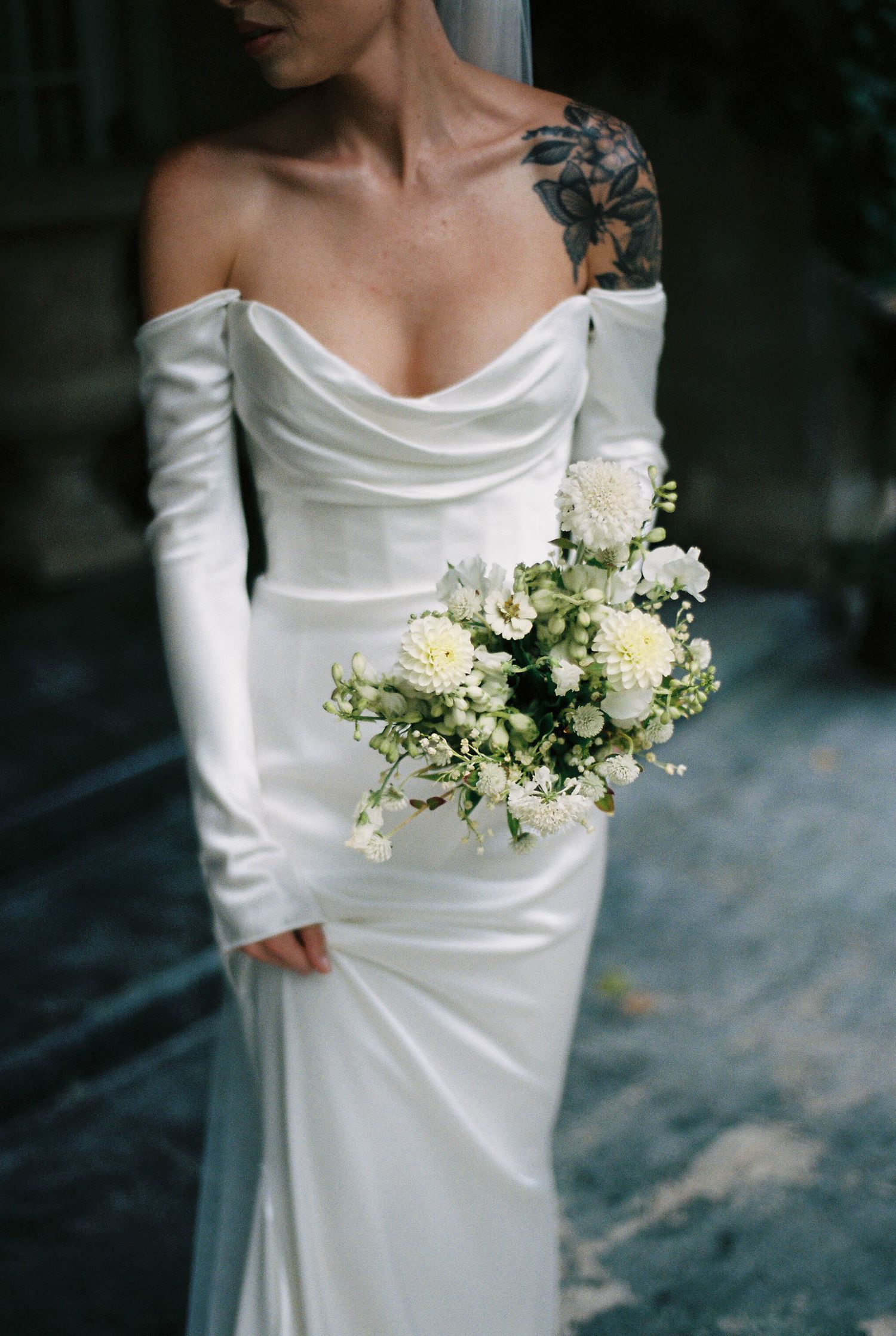 Modern wedding dress with off-shoulder design and white floral bouquet.