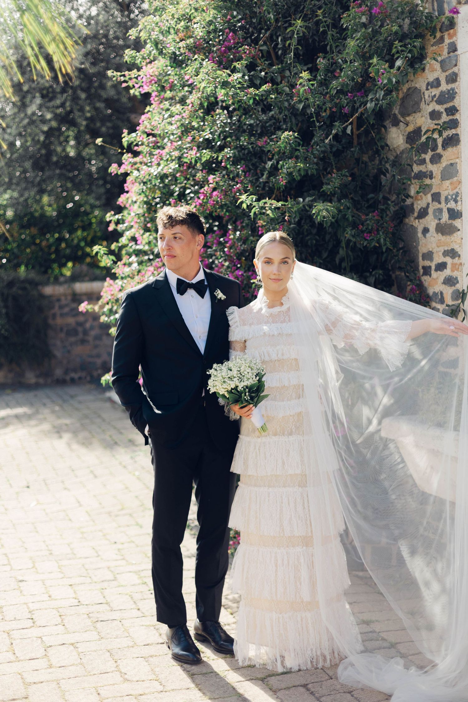 Elegant wedding portrait with couple standing against stone wall and pink flowering vines at castello della castellucia in rome italy.