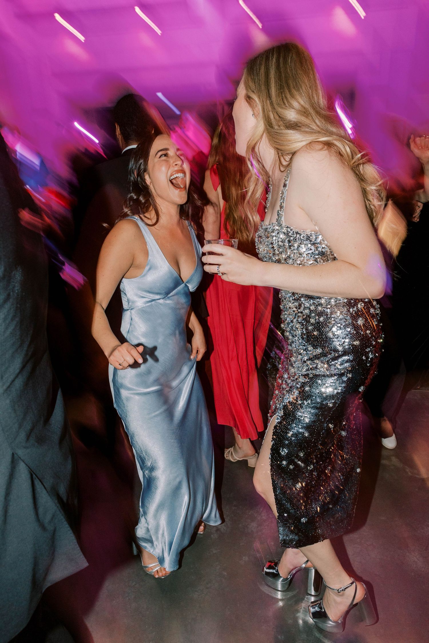 Two wedding guests dancing and laughing together under purple party lights.