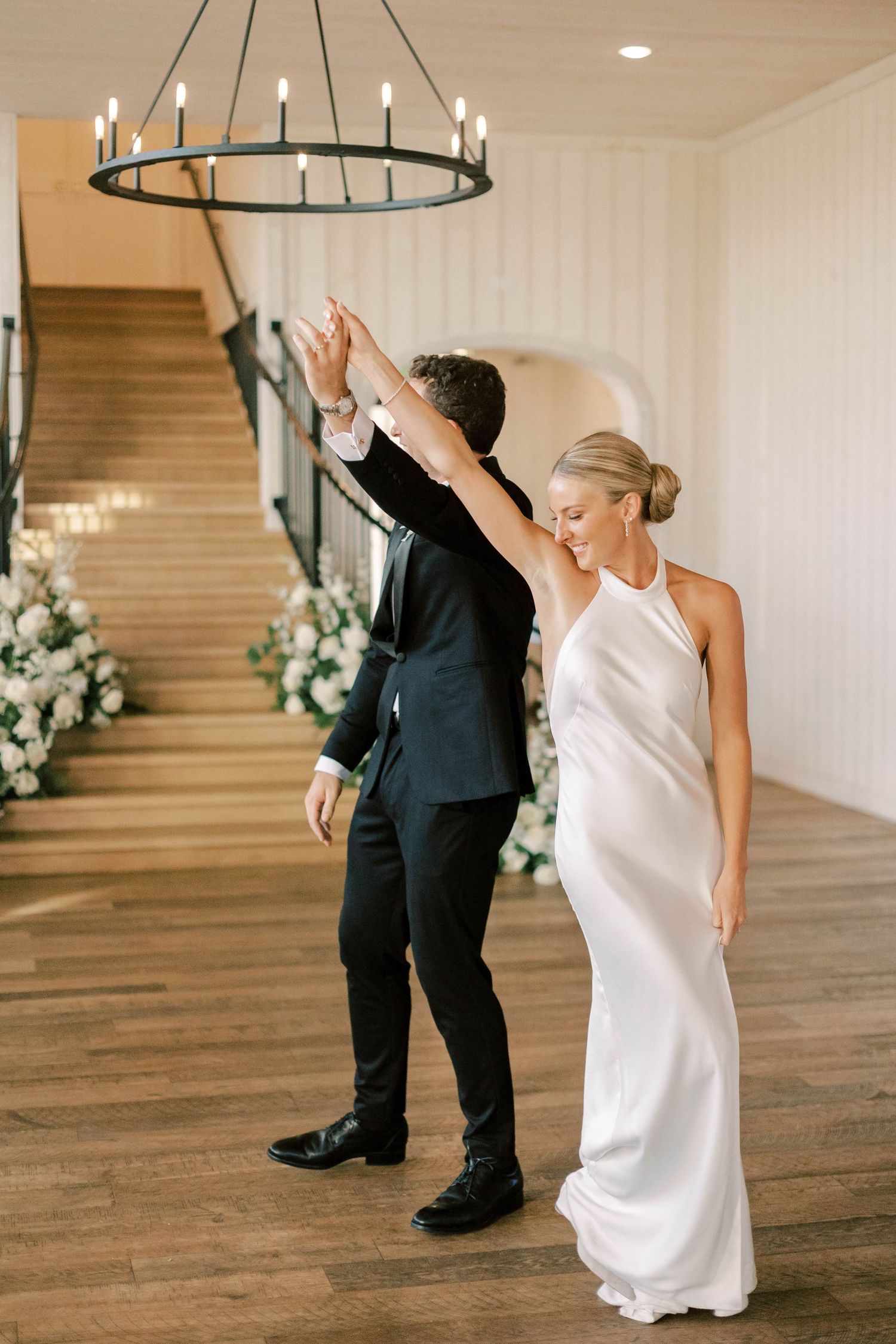 A couple performing a dance move under an elegant chandelier in a white-walled venue.