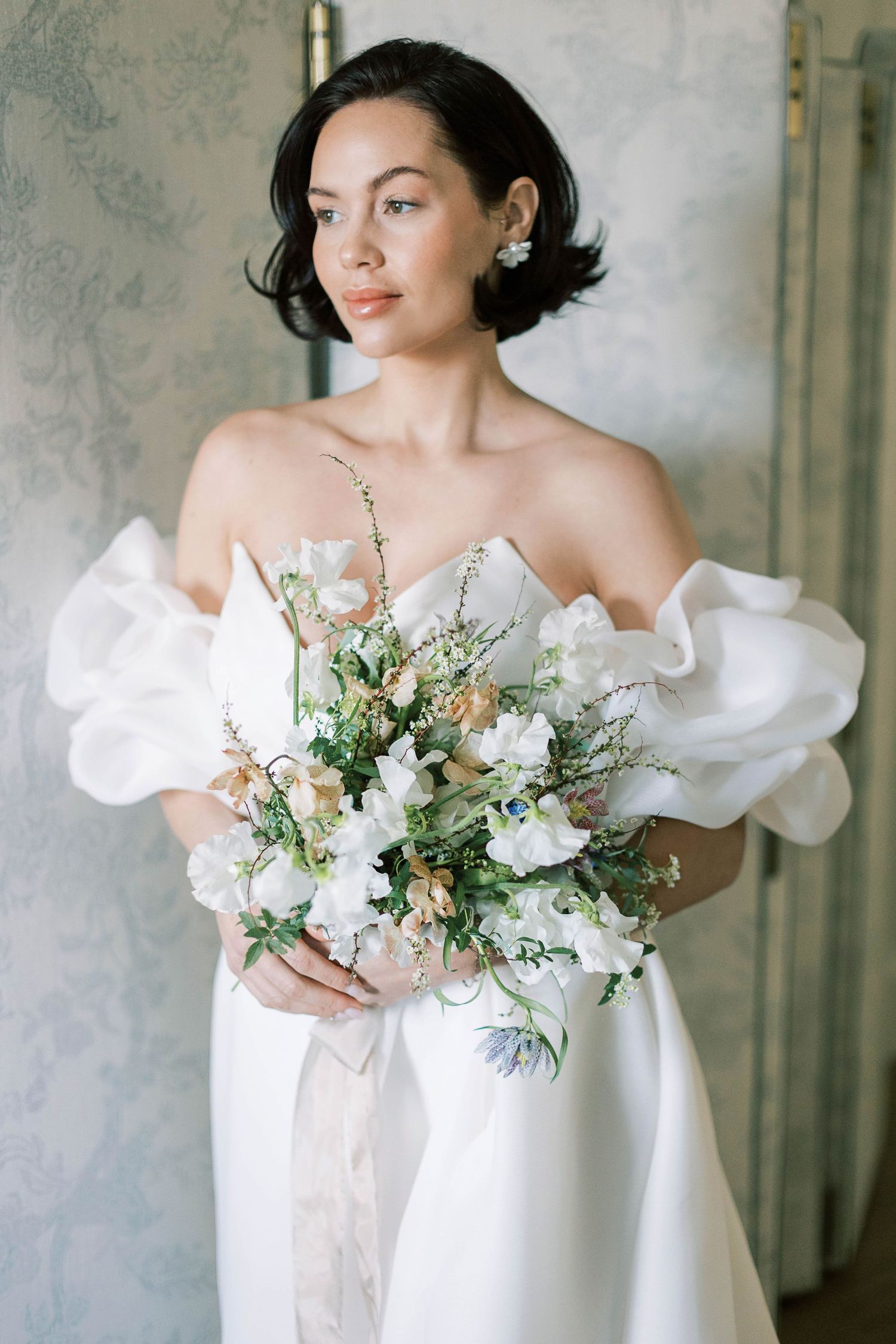 Elegant bridal portrait featuring white off-shoulder gown and lush white and green bouquet.
