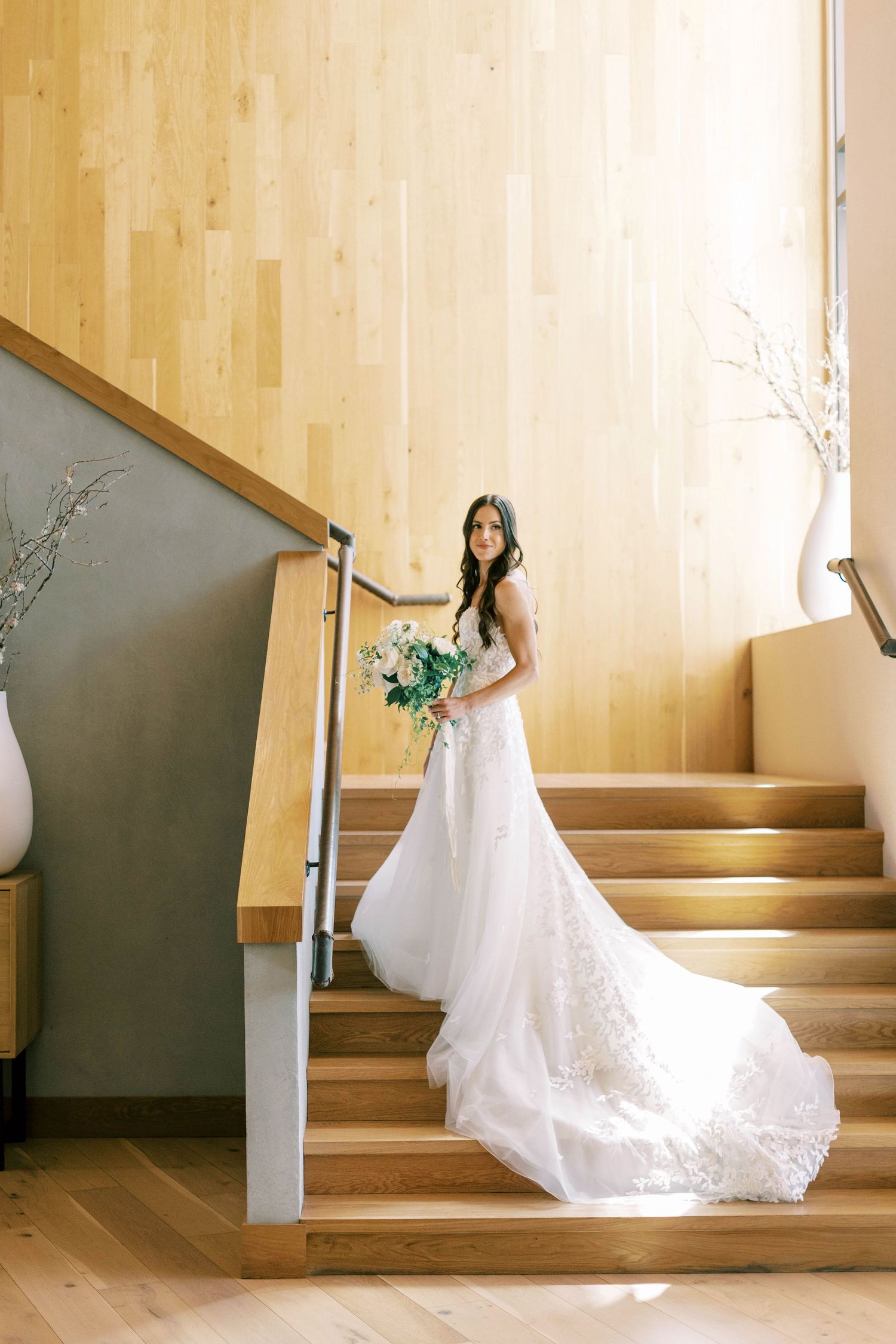 Bride in a stunning lace wedding gown poses elegantly on wooden stairs of blue sky.