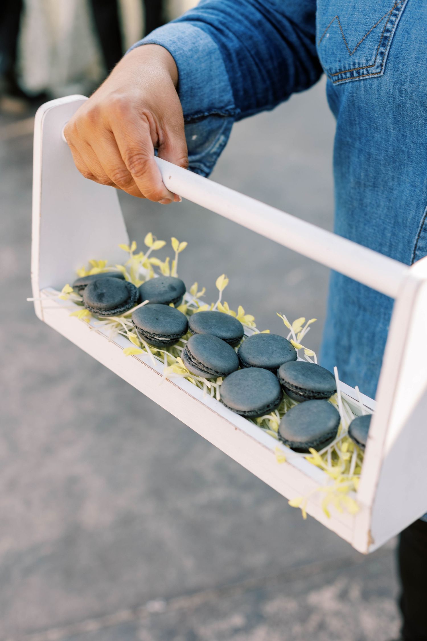 Dark macarons displayed on a white wooden serving tray with delicate yellow garnish.
