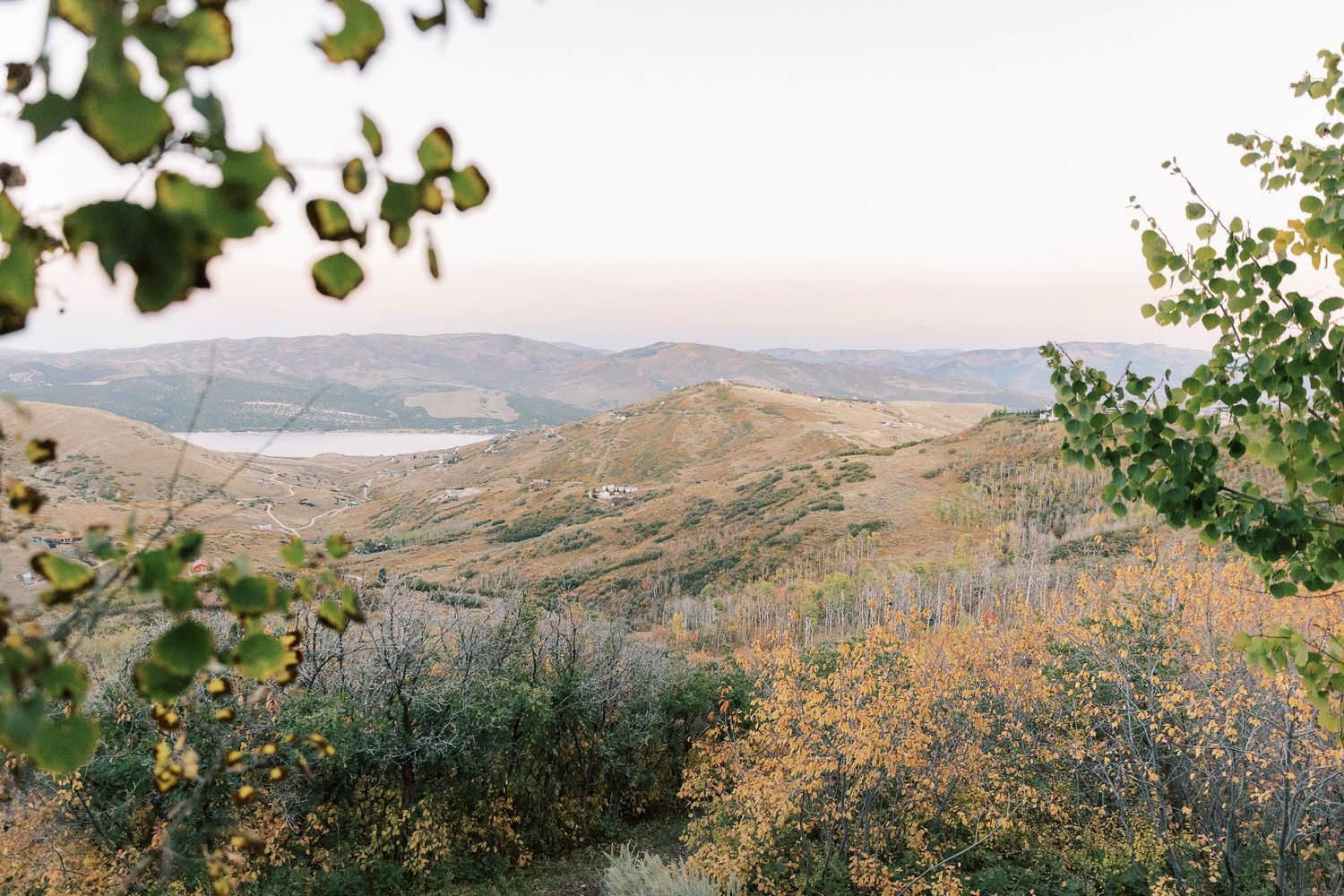 Rolling hills and mountains stretch into the distance under a soft sunset sky with green foliage in the foreground of promontory club.