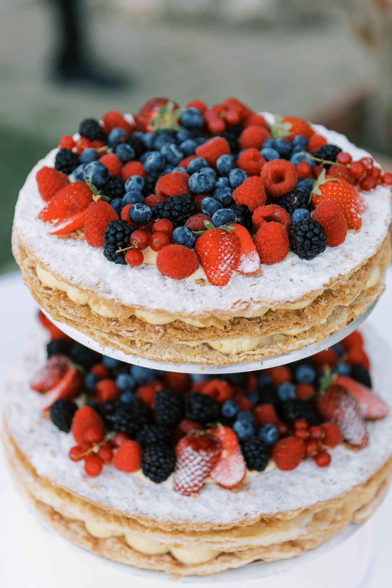 Two-tiered mille-feuille cake decorated with fresh strawberries, blueberries, and blackberries at wedding in rome.