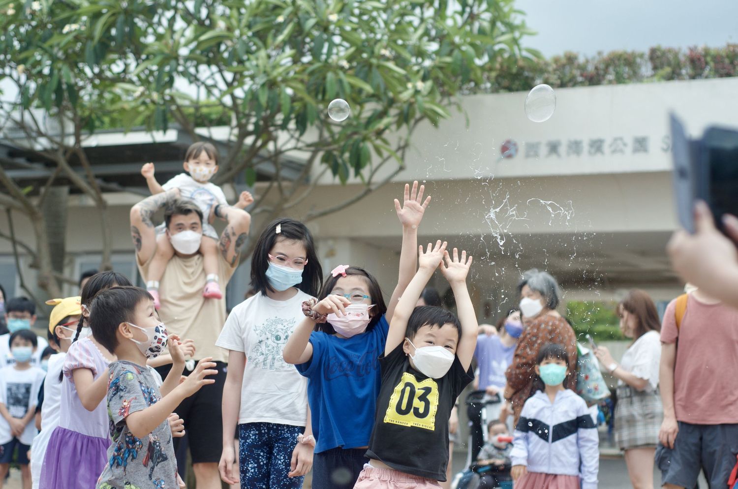 Group reaching for bubbles floating through the air at an outdoor event.