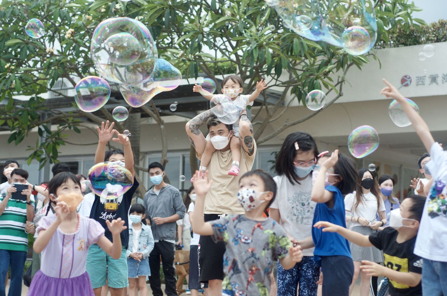 Group of people in masks blowing bubbles outdoors during daytime activities.
