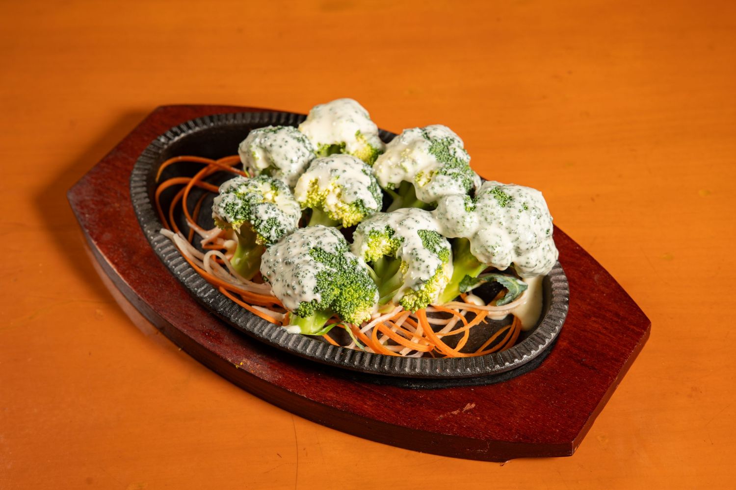 Steaming hot broccoli served on a sizzling cast iron platter with garnishes on a wooden surface.