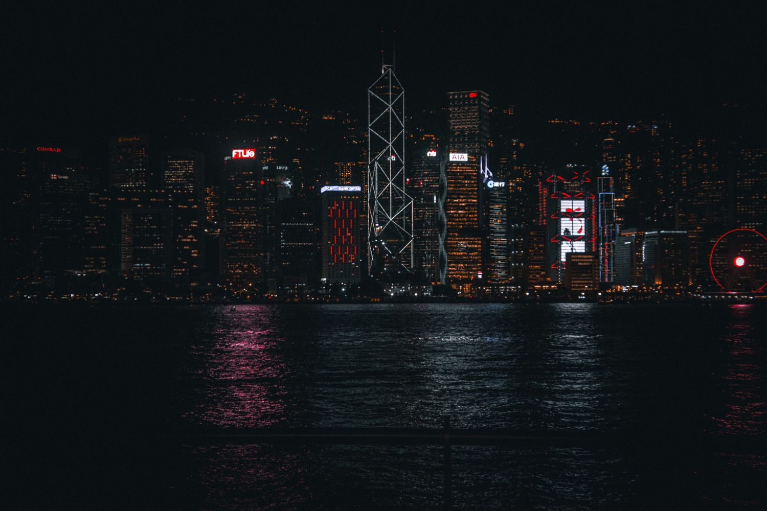 Hong Kong skyline at night reflecting on Victoria Harbor with illuminated skyscrapers.