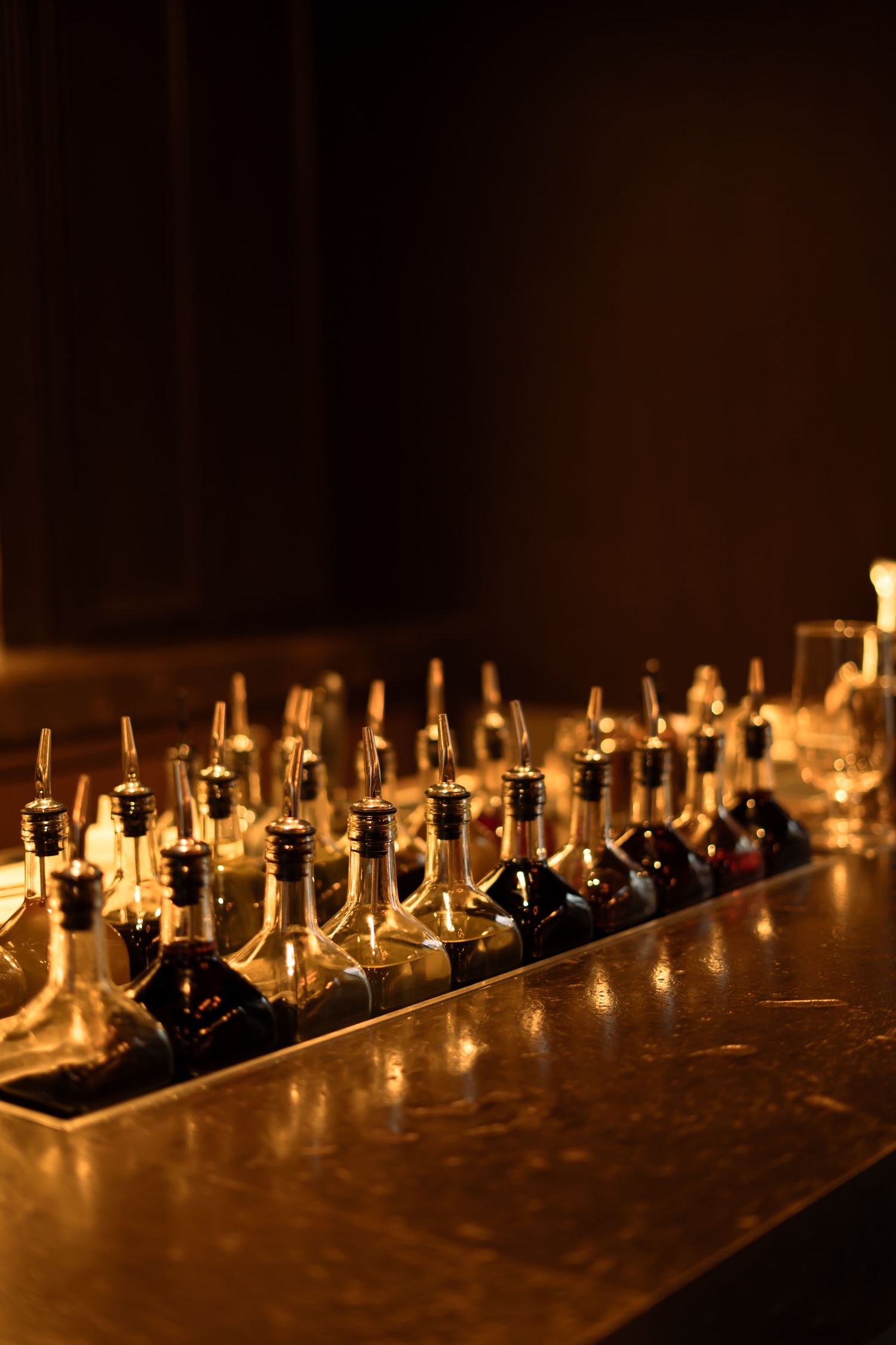 Multiple wine bottles with lights arranged in a row on a dark wooden bar counter create a warm, glowing ambiance.