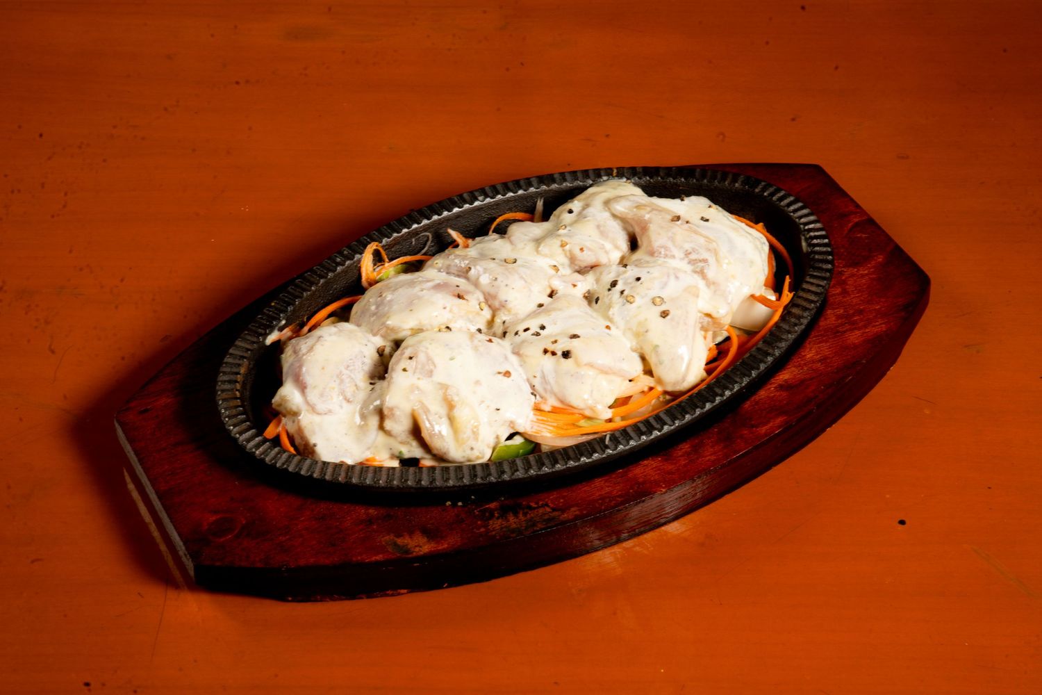 A sizzling fajita platter with grilled chicken and onions served on a wooden base with a cast iron skillet.