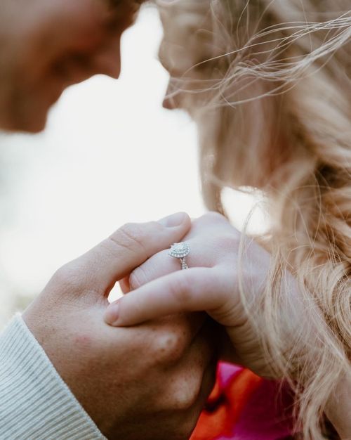 Close up of hands showing engagement ring in soft lighting.
