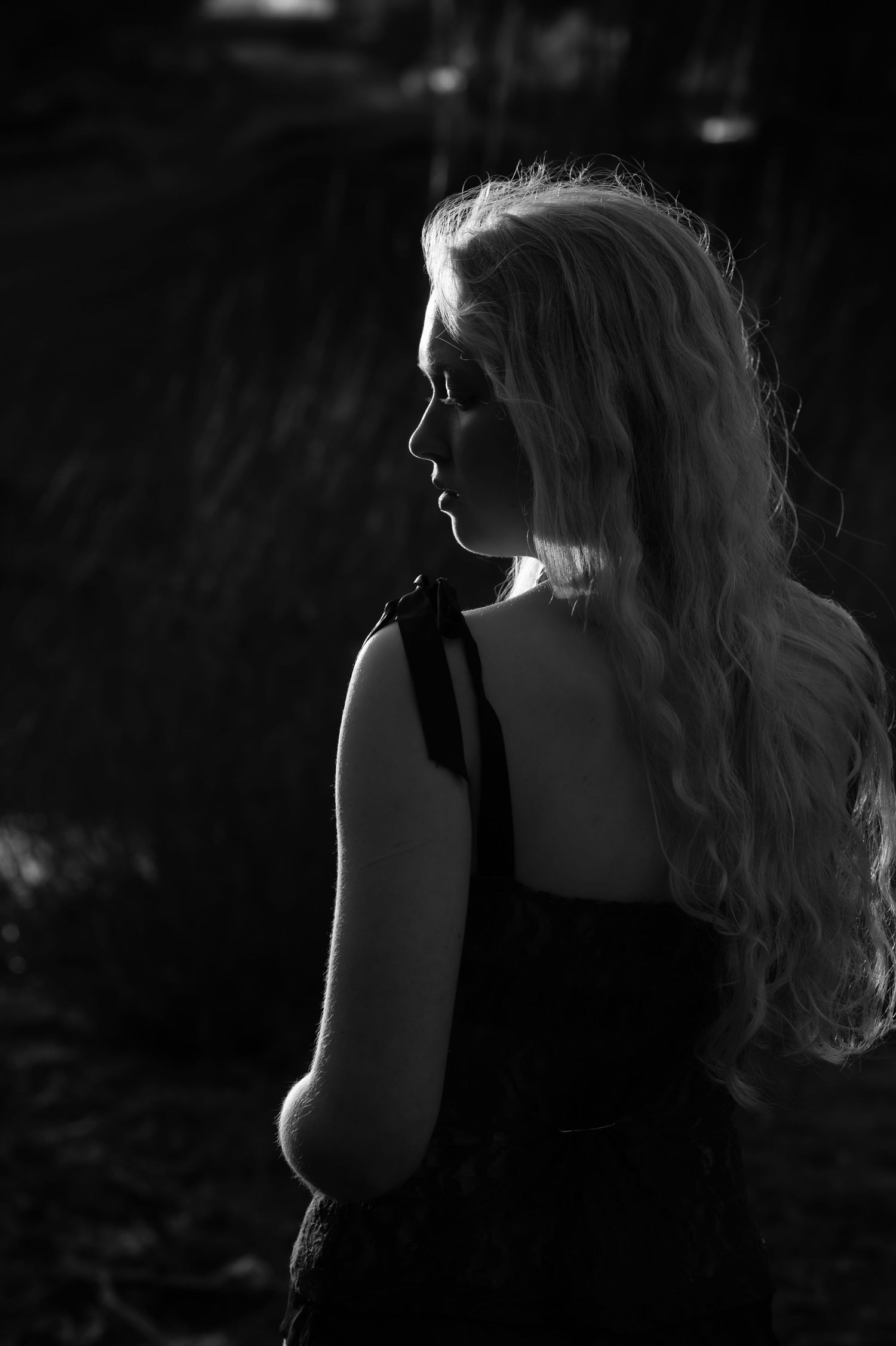 artistic black and white senior portrait of a young woman's silhouette, sidelit by sunlight against a black background