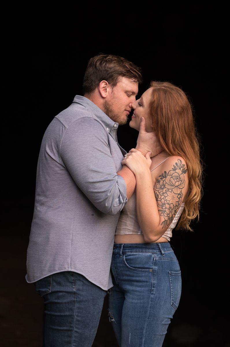 a young couple kisses with a black background behind them