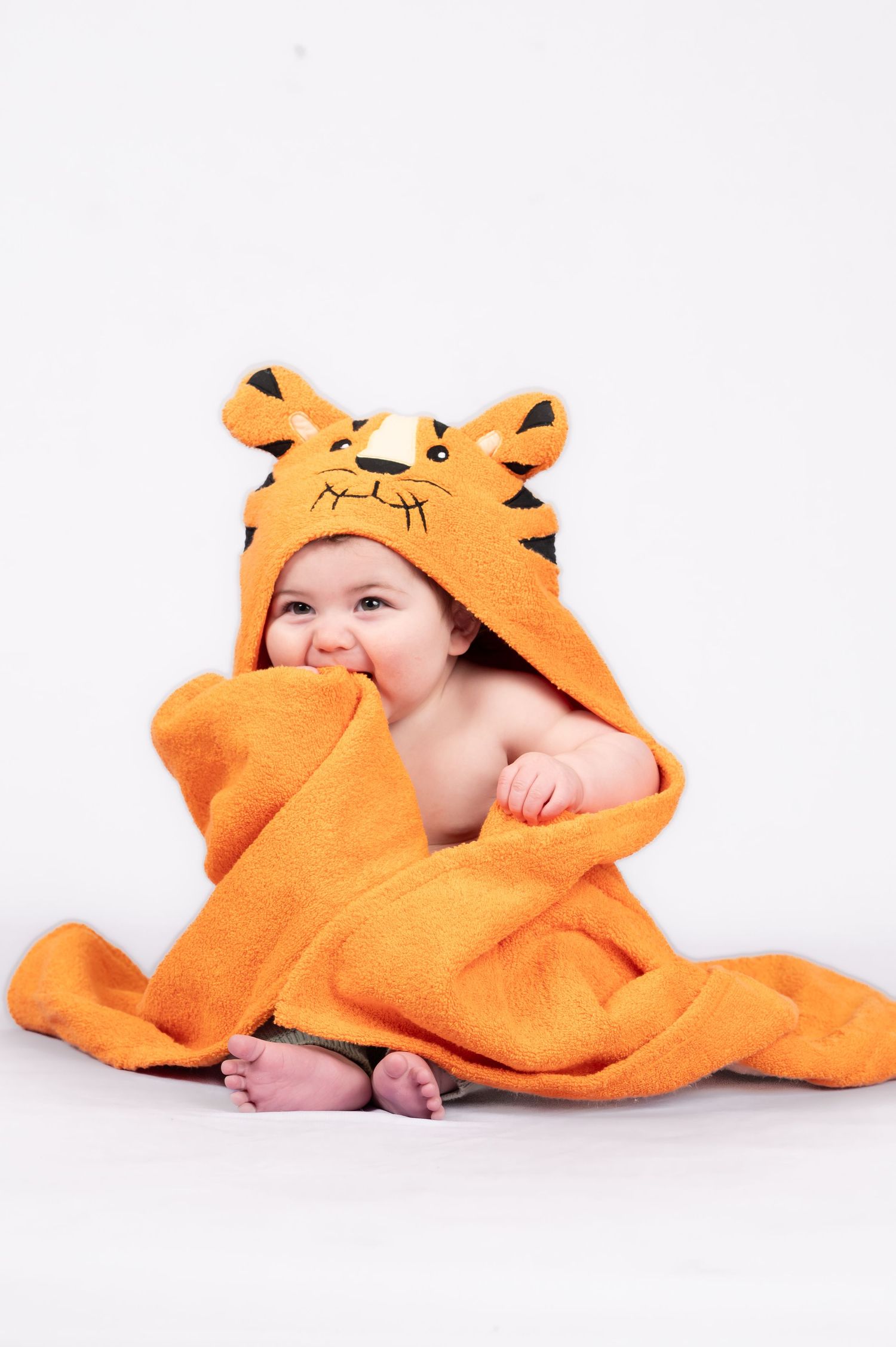 commercial product shot of a baby boy wrapped in a bright orange tiger bath towel on a white studio background