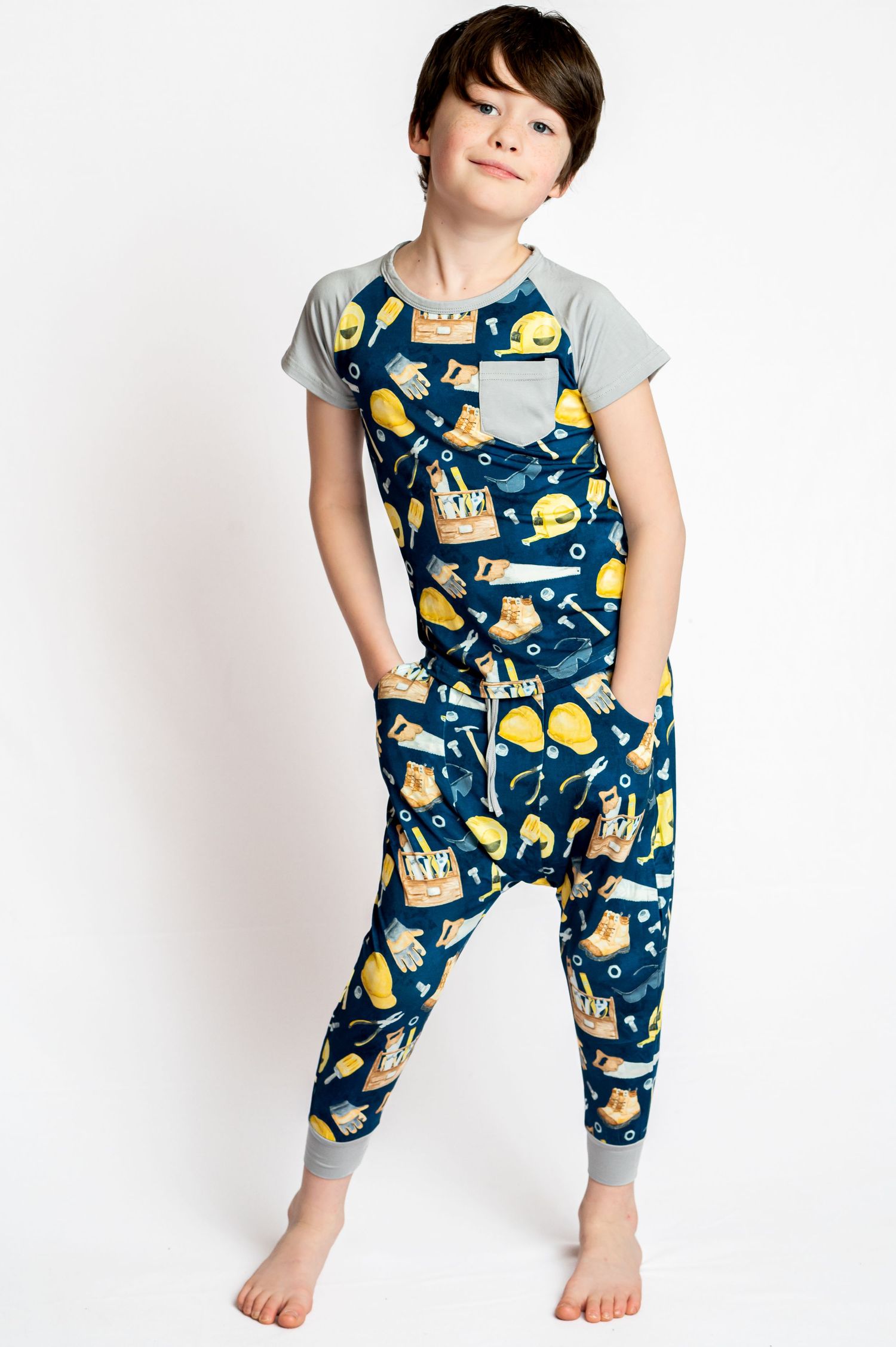 a young boy models a pair of navy blue and gray pajamas while standing on a white studio backdrop