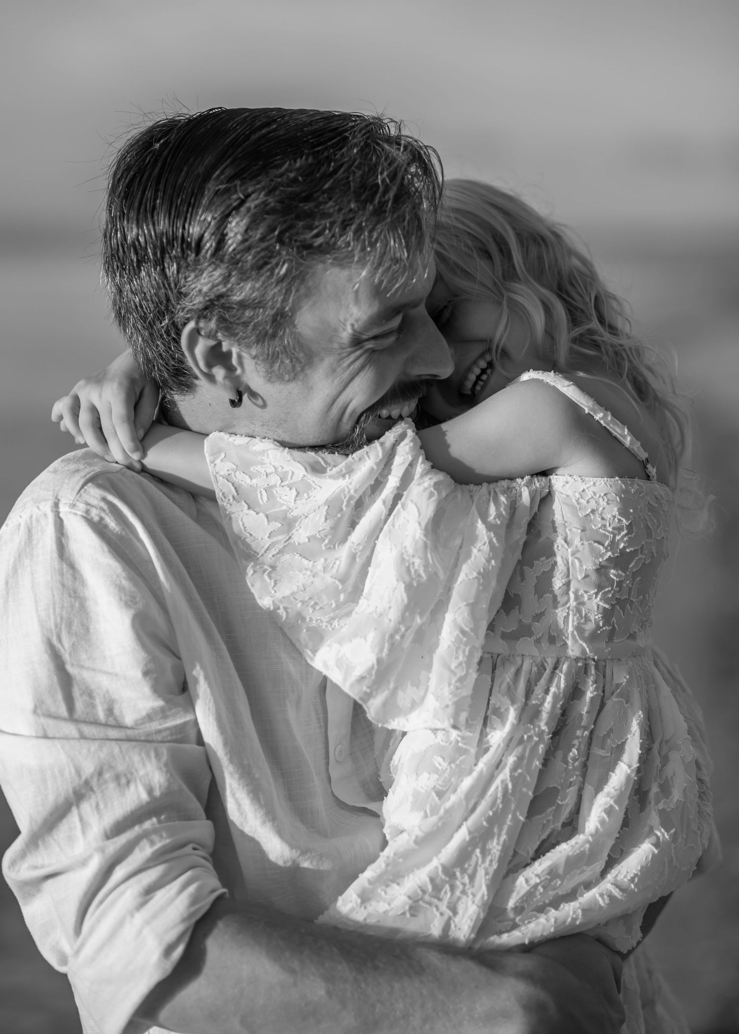 black and white candid closeup shot of a father and his little girl hugging and laughing together