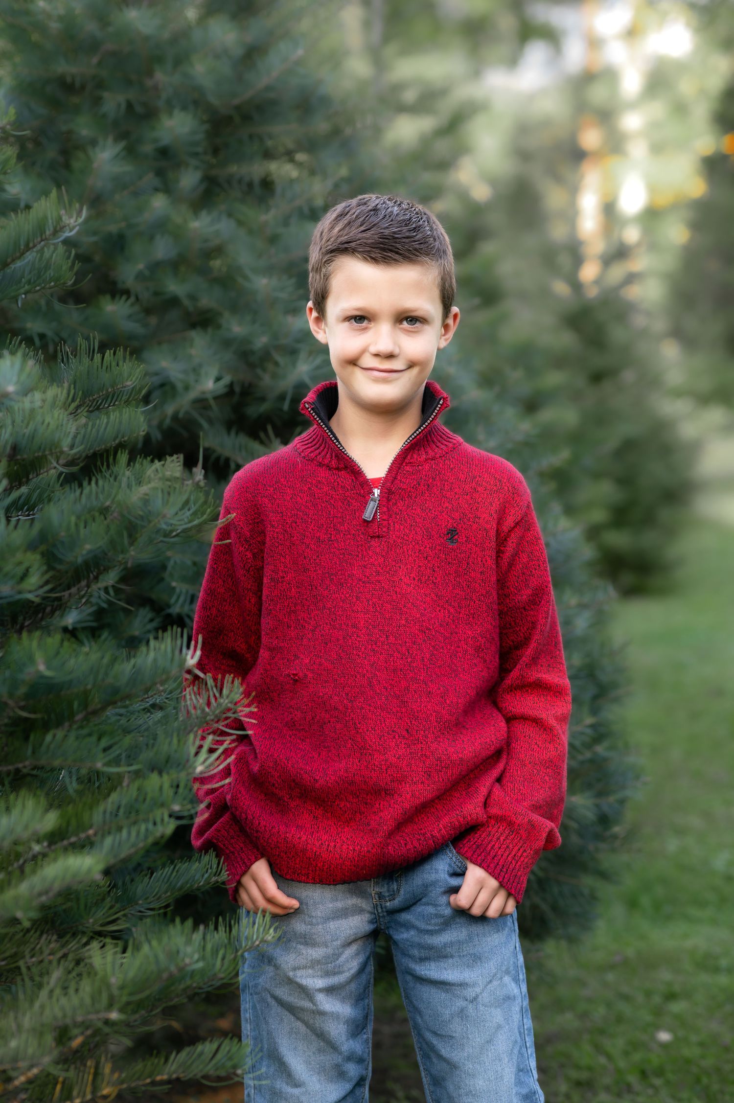 a young boy in a bright red Christmas sweater poses and smiles for a Christmas portrait on a Christmas tree farm in Fairmont, WV