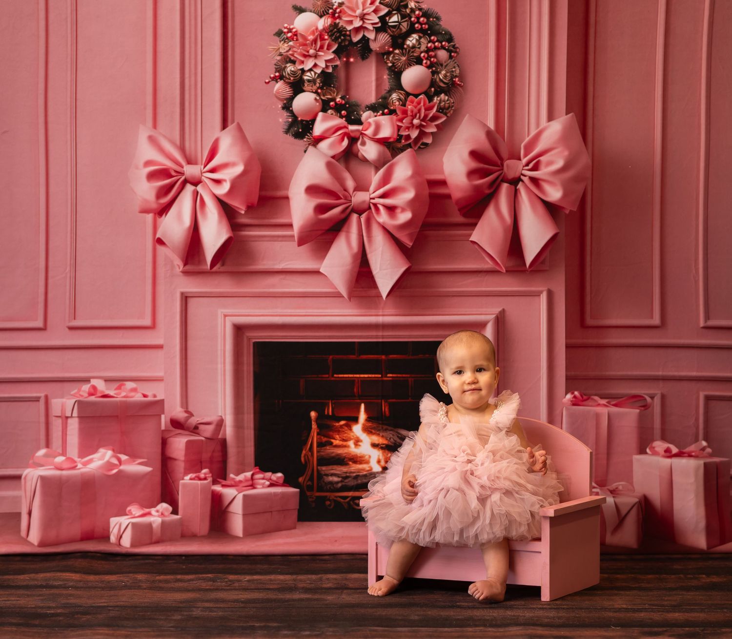 a baby girl in a fluffy pink tulle dress poses in a pink chair in a Pink Christmas room filled with pink bows and gifts