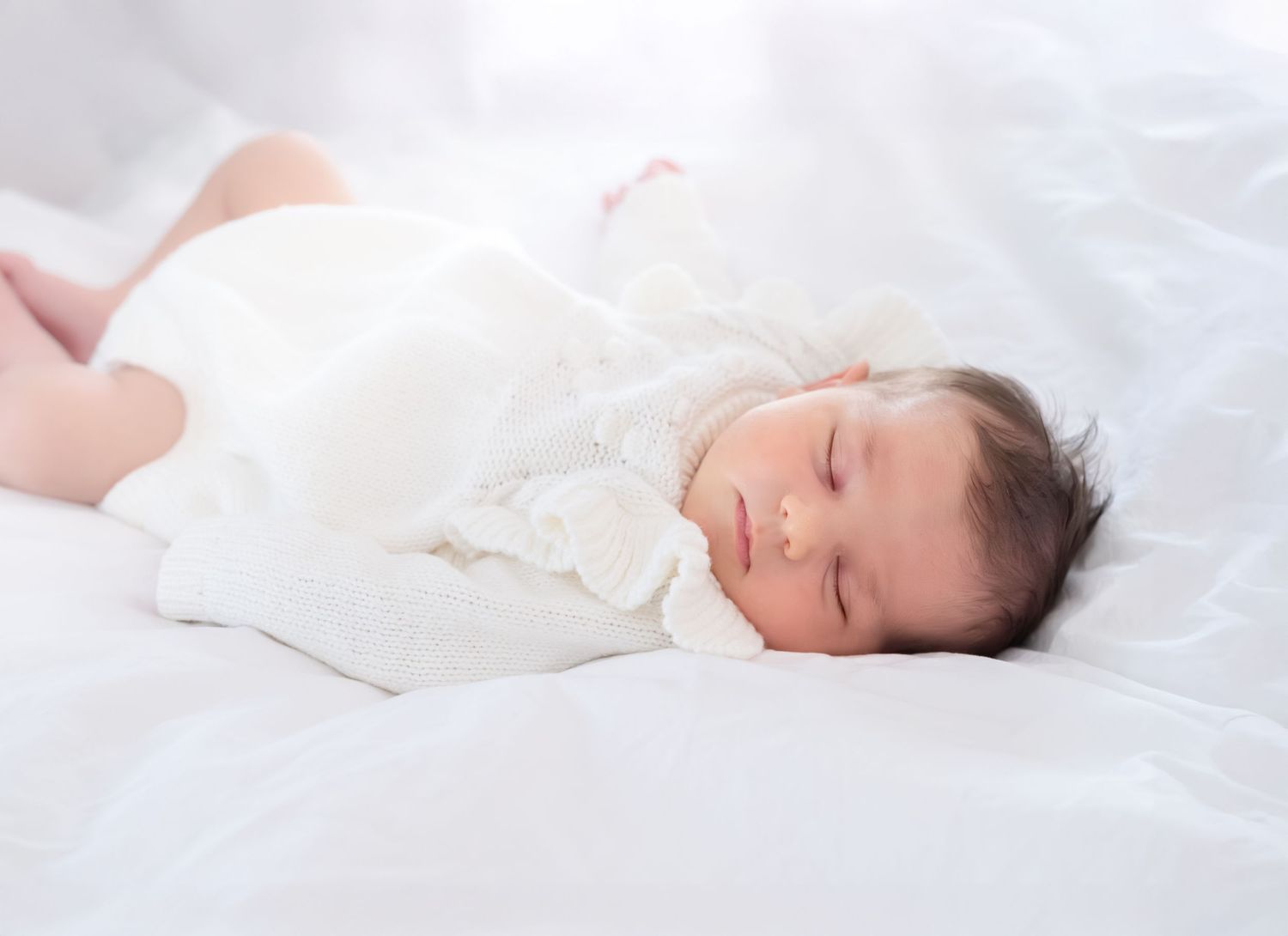 a newborn baby dressed in all white lies on a fluffy white blanket