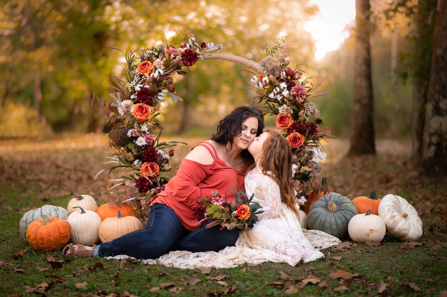 a mother and daughter pose in an autumn setting with pumpkins all around and a fall floral hoop in the background, in St. Albans, WV