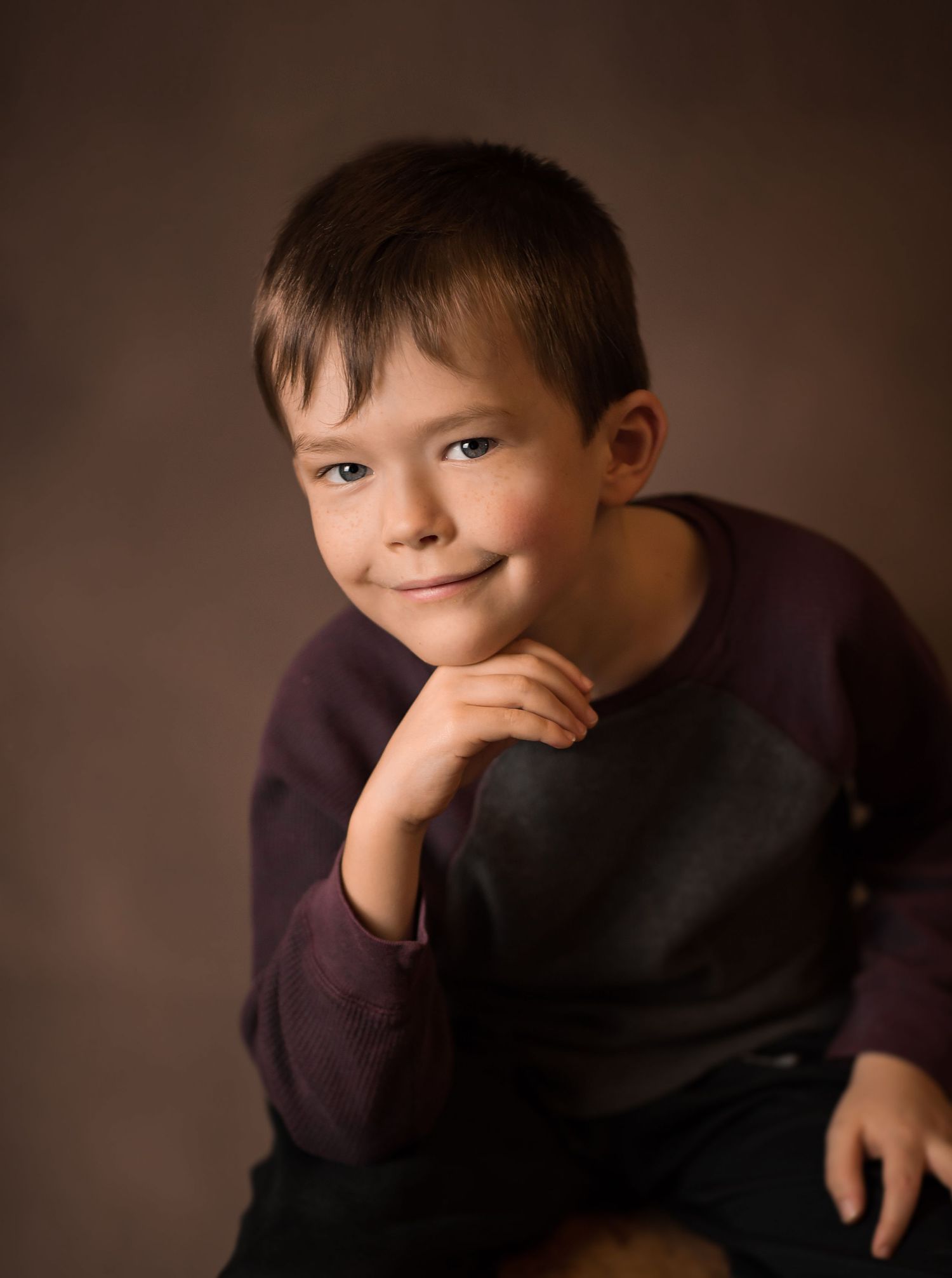 an old master's style studio portrait of a little boy posing with his chin on his hand and smiling for the camera