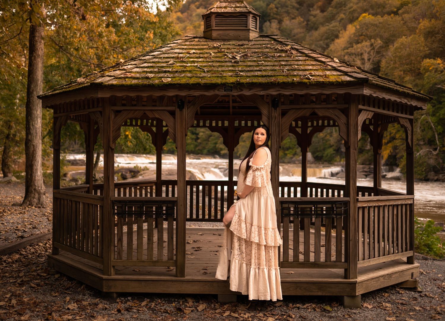 a dark haired pregnant woman in a long lacy beige gown stands at the door of a gazebo in Valley Falls State Park, WV