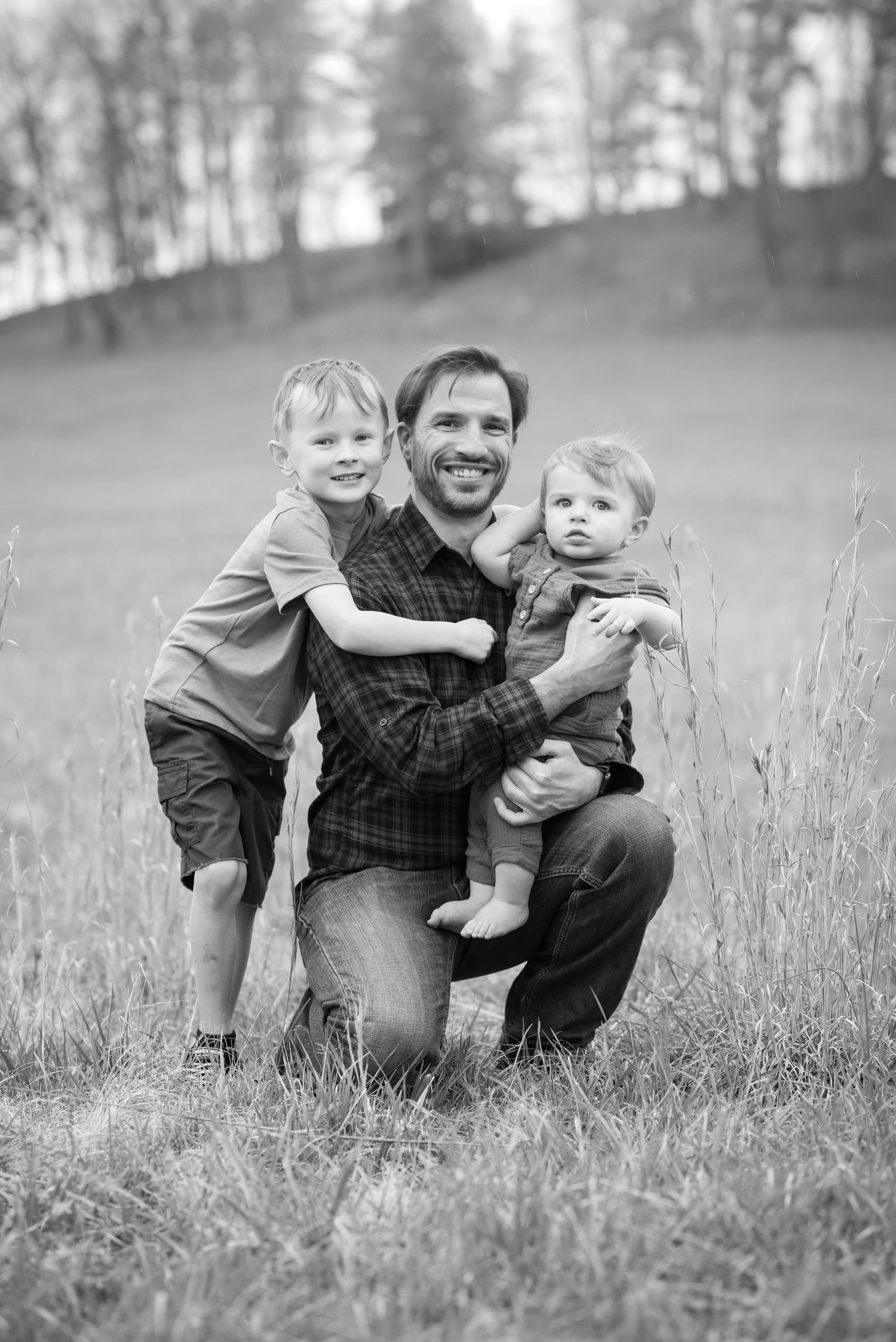 a man kneels in a field to pose with his arms around his two young nephews