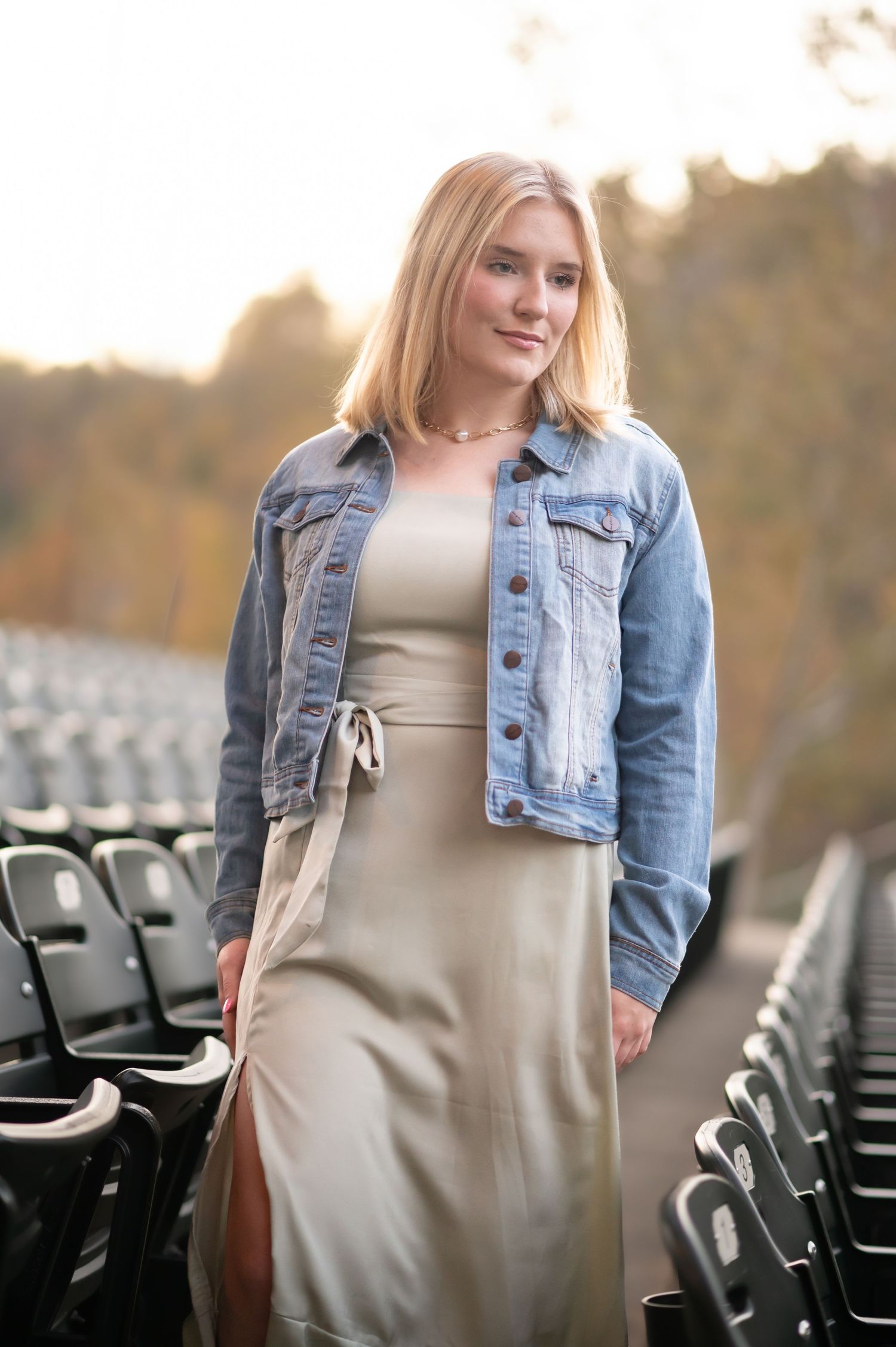 a young blonde woman in a green dress and denim jacket walks between rows of empty stadium seating