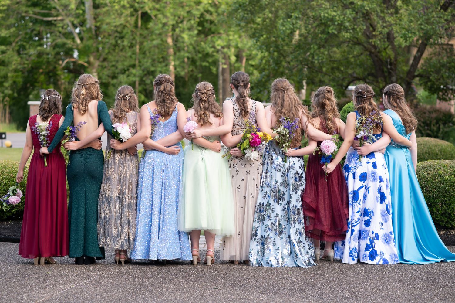 a group of teenage girls in prom dresses pose for a fun portrait with arms around each other, facing away