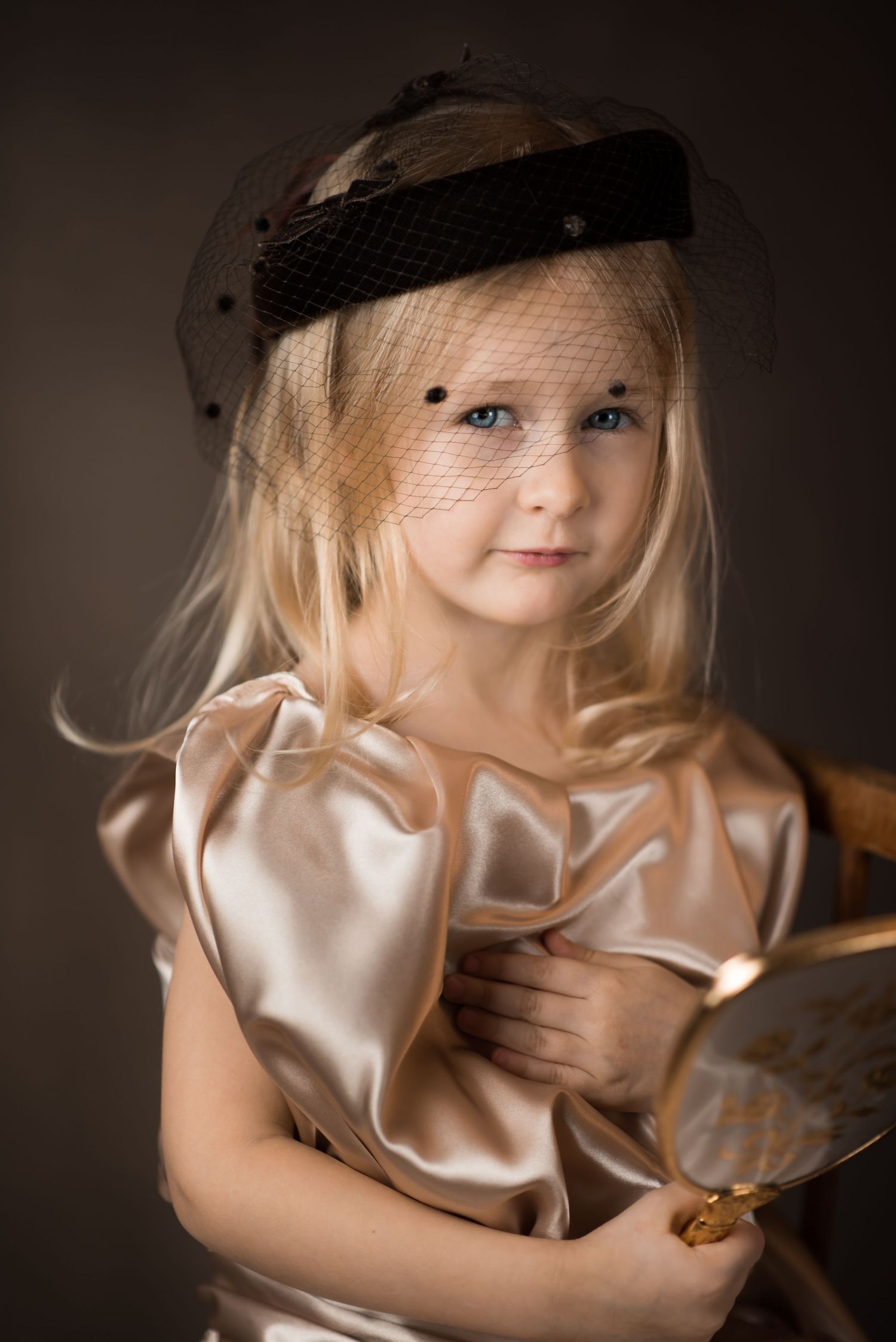 classical old master's style portrait of a little blonde girl in a 1920's hat and gold dress, holding a vintage hand mirror