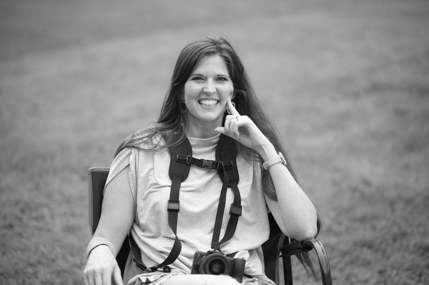 black and white of photographer Laura Priestley wearing her camera gear, sitting in a chair and laughing