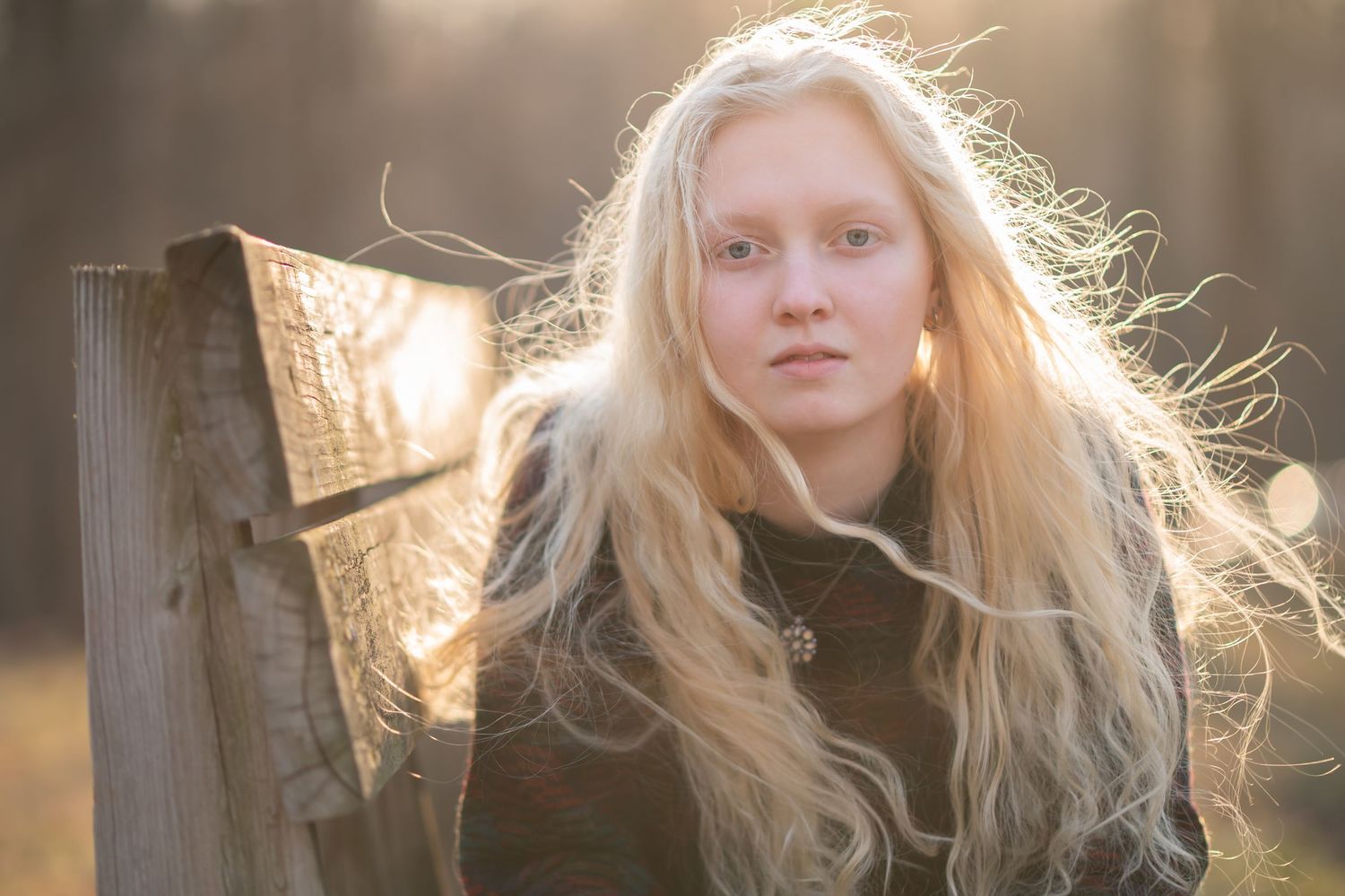 closeup senior portrait of a young woman with long blonde hair; she leans on her elbows on a bench and looks into the camera