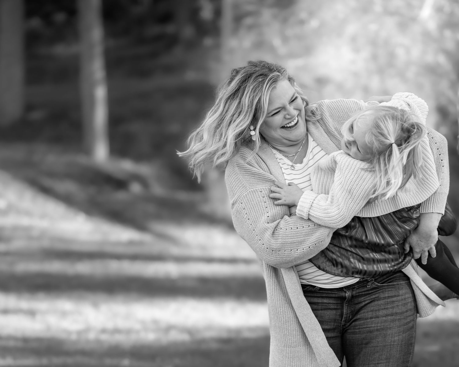 black and white candid shot of a mother twirling her daughter around in a field and laughing