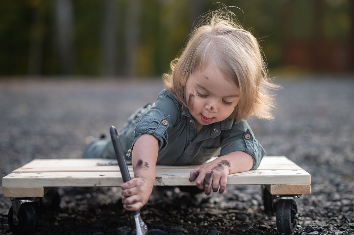 a little boy in a mechanic uniform with grease on his face lies on a scooter holding a large wrench
