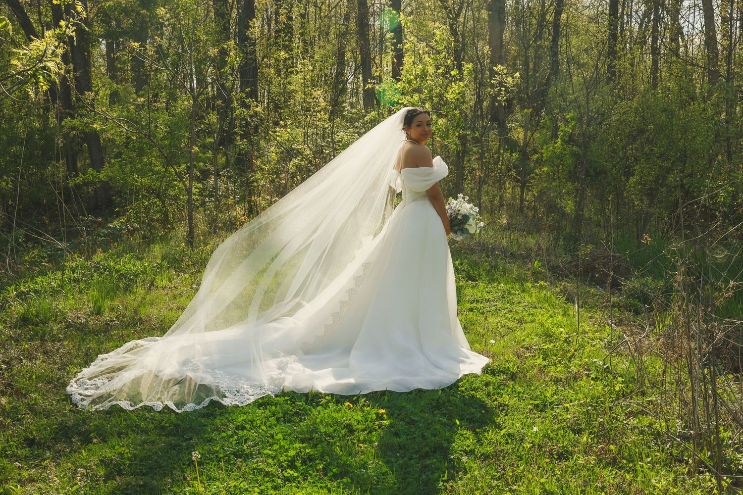 A flowing white wedding dress twirls through a sunlit forest path creating an ethereal outdoor bridal scene.
