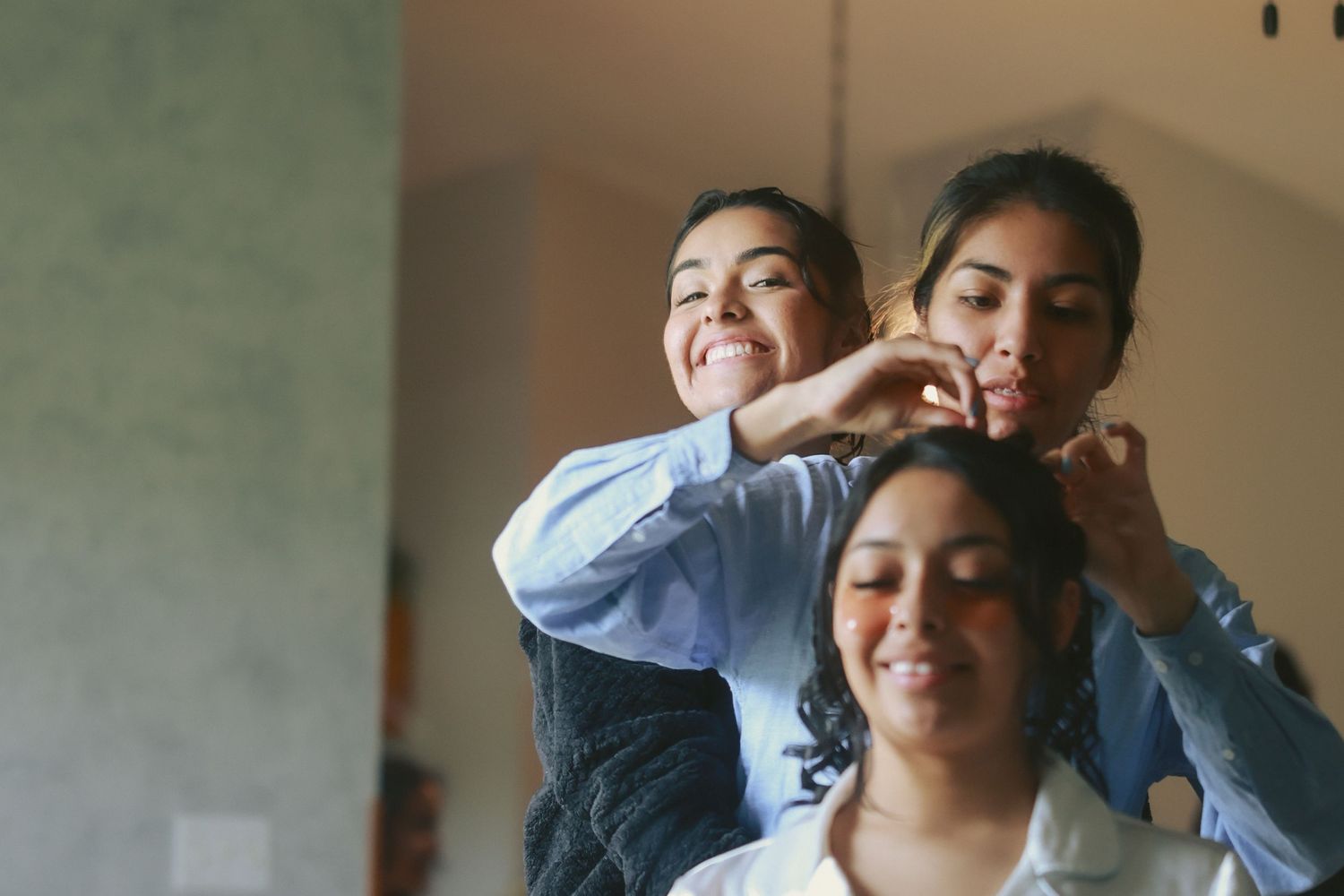 Three people smile and laugh playfully together while getting ready indoors.