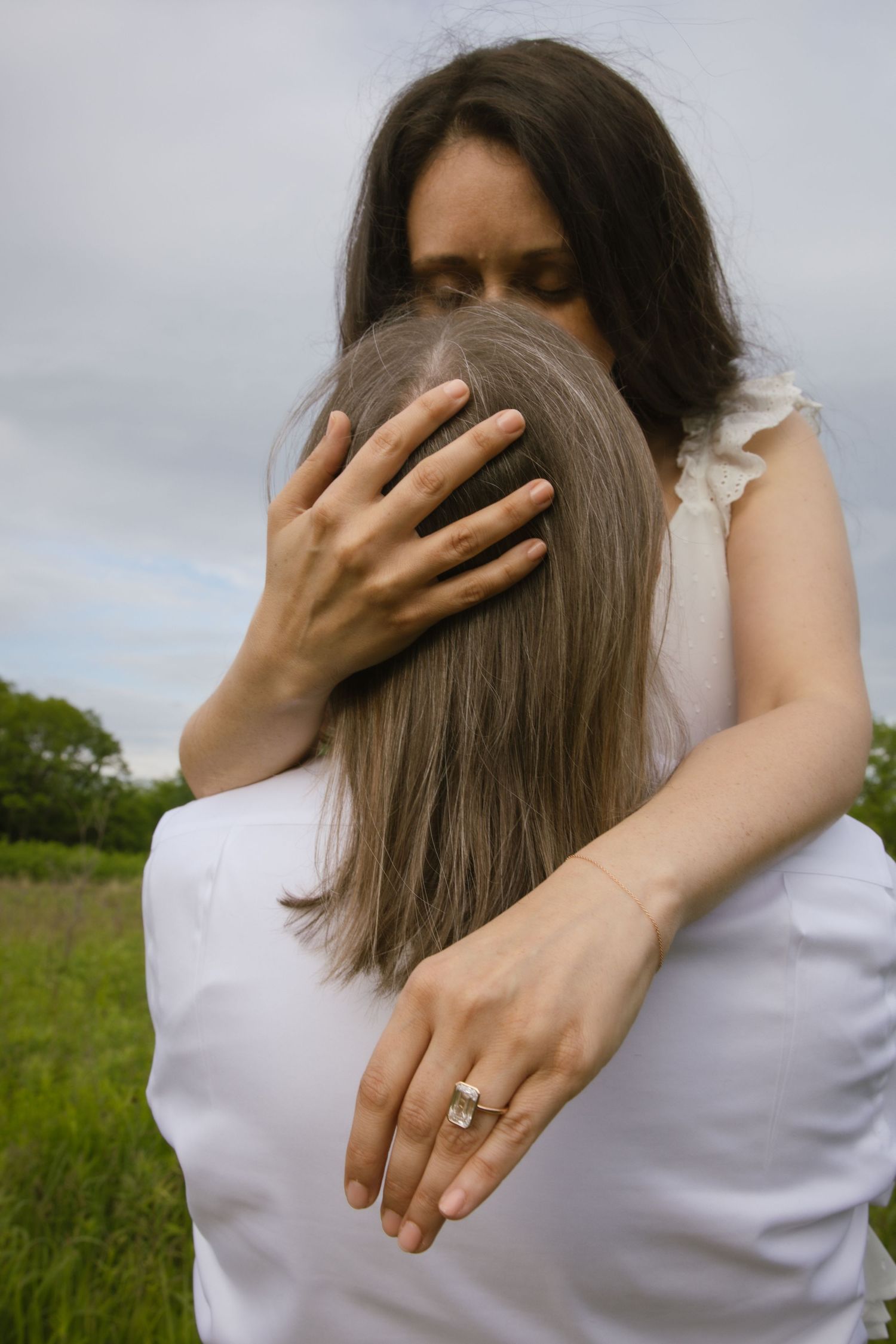 Two people embracing in a tender moment outdoors with one person's hand displaying an engagement ring.