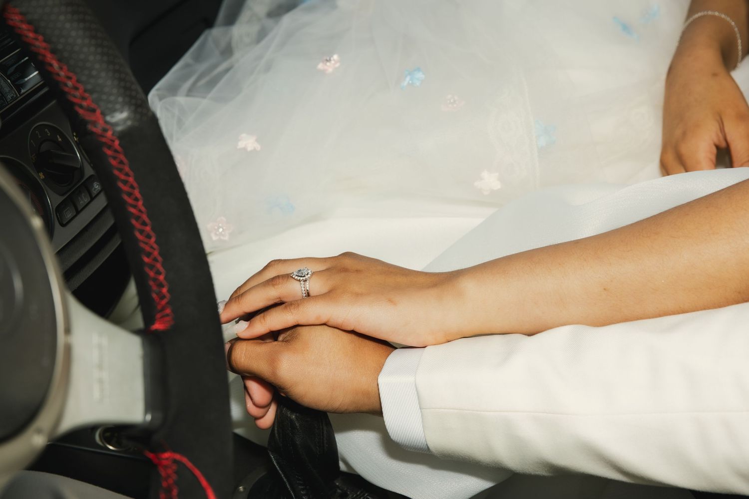 Close up of hands wearing wedding rings resting on white fabric against a dark car interior panel.